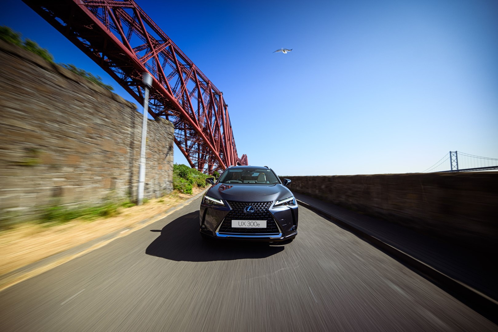Lexus UX300e con puente de estructura metálica de fondo, enfatizando su aspecto aerodinámico.