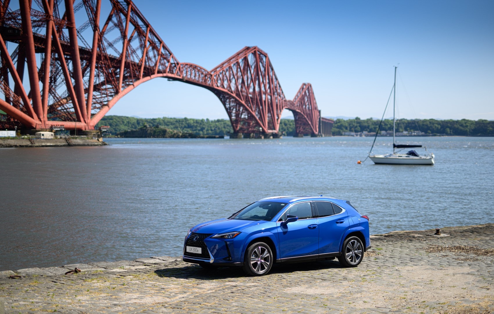 Lexus UX300e con vista lateral, estacionado frente a un paisaje con puente.