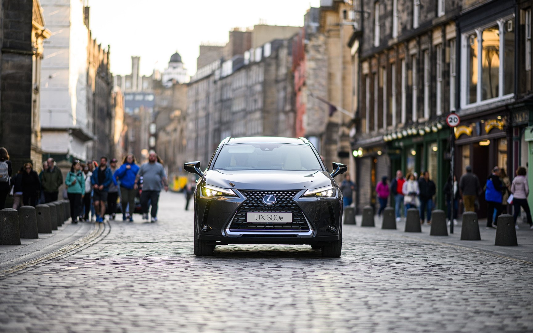 Frontal del Lexus UX300e en una escena urbana con peatones al fondo, destacando su presencia en ciudad.