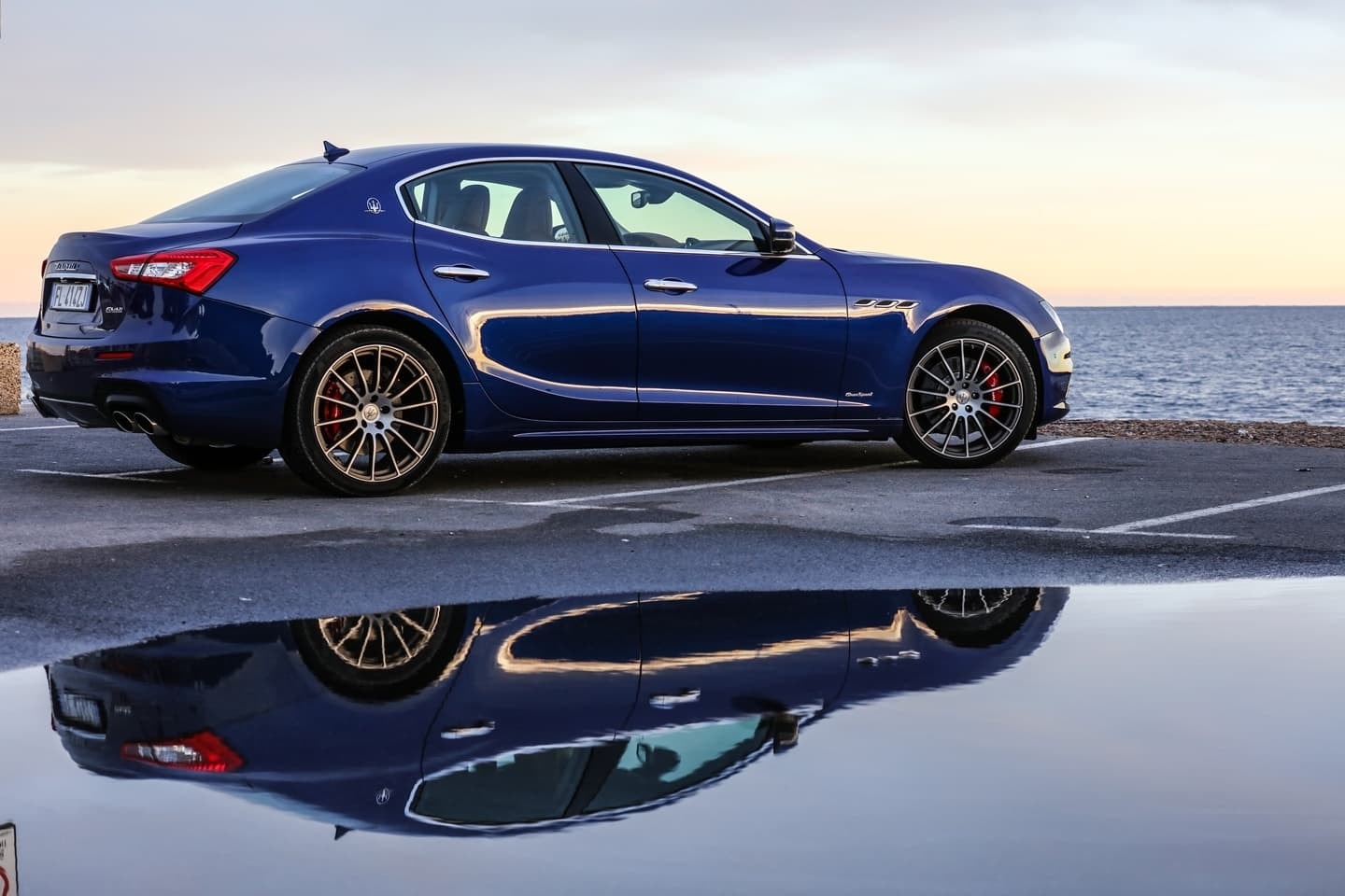 Perfil del Maserati Ghibli reflejándose en la superficie mojada al atardecer.