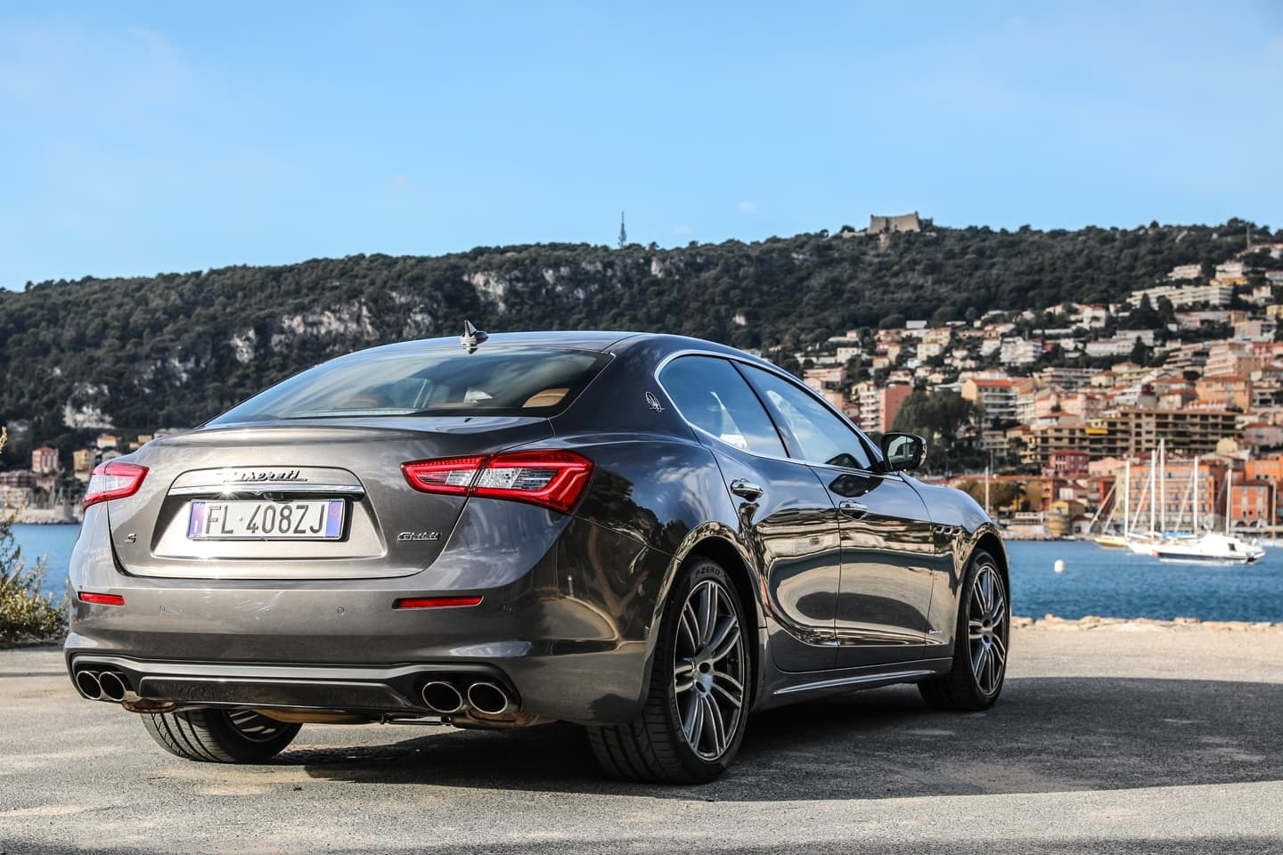 Vista trasera y lateral de un Maserati Ghibli estacionado con paisaje urbano al fondo
