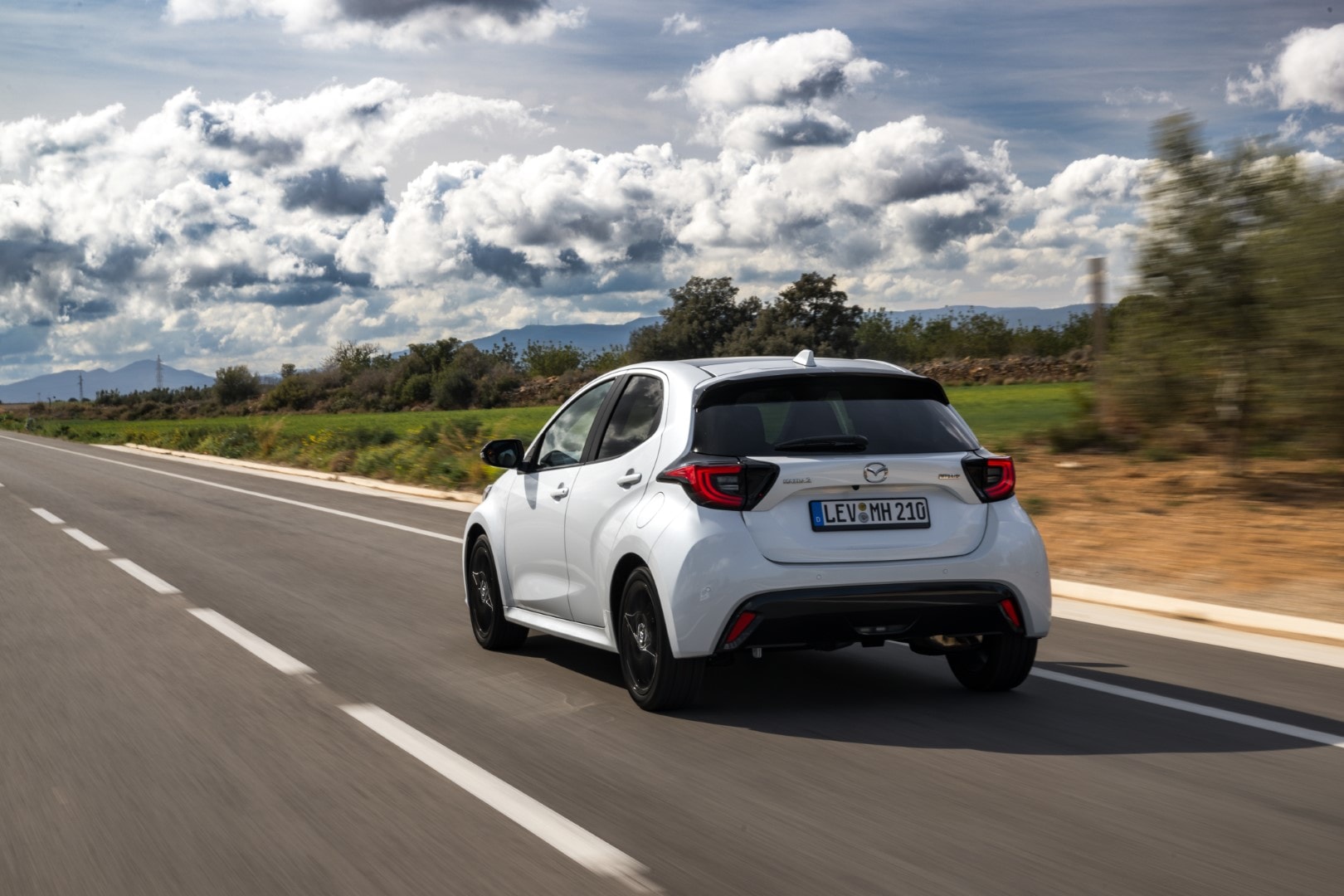 Muestra el Mazda 2 híbrido desde un ángulo lateral trasero en movimiento, realzando su diseño trasero.