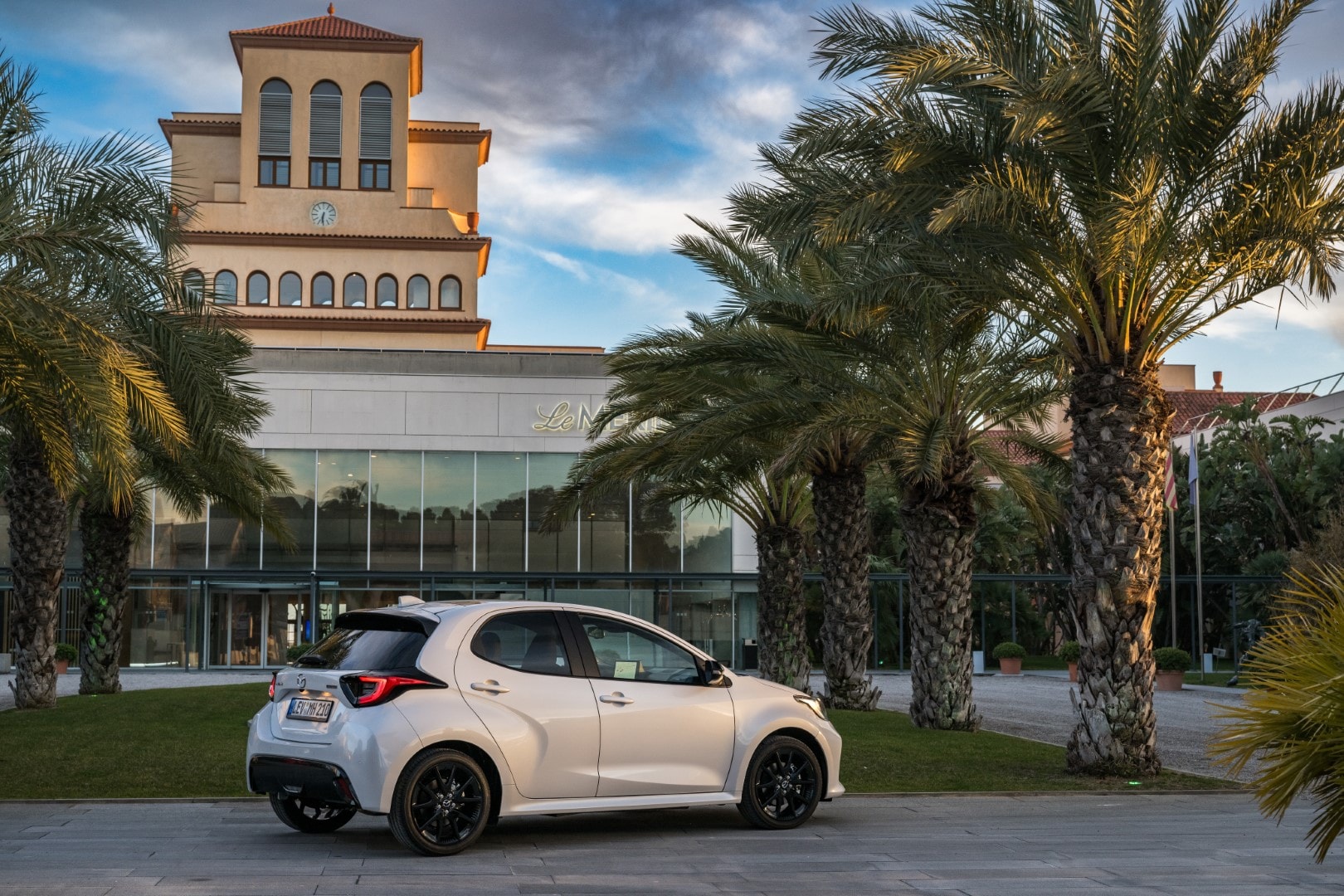 Vista trasera y lateral del Mazda 2 híbrido con un entorno urbano al atardecer