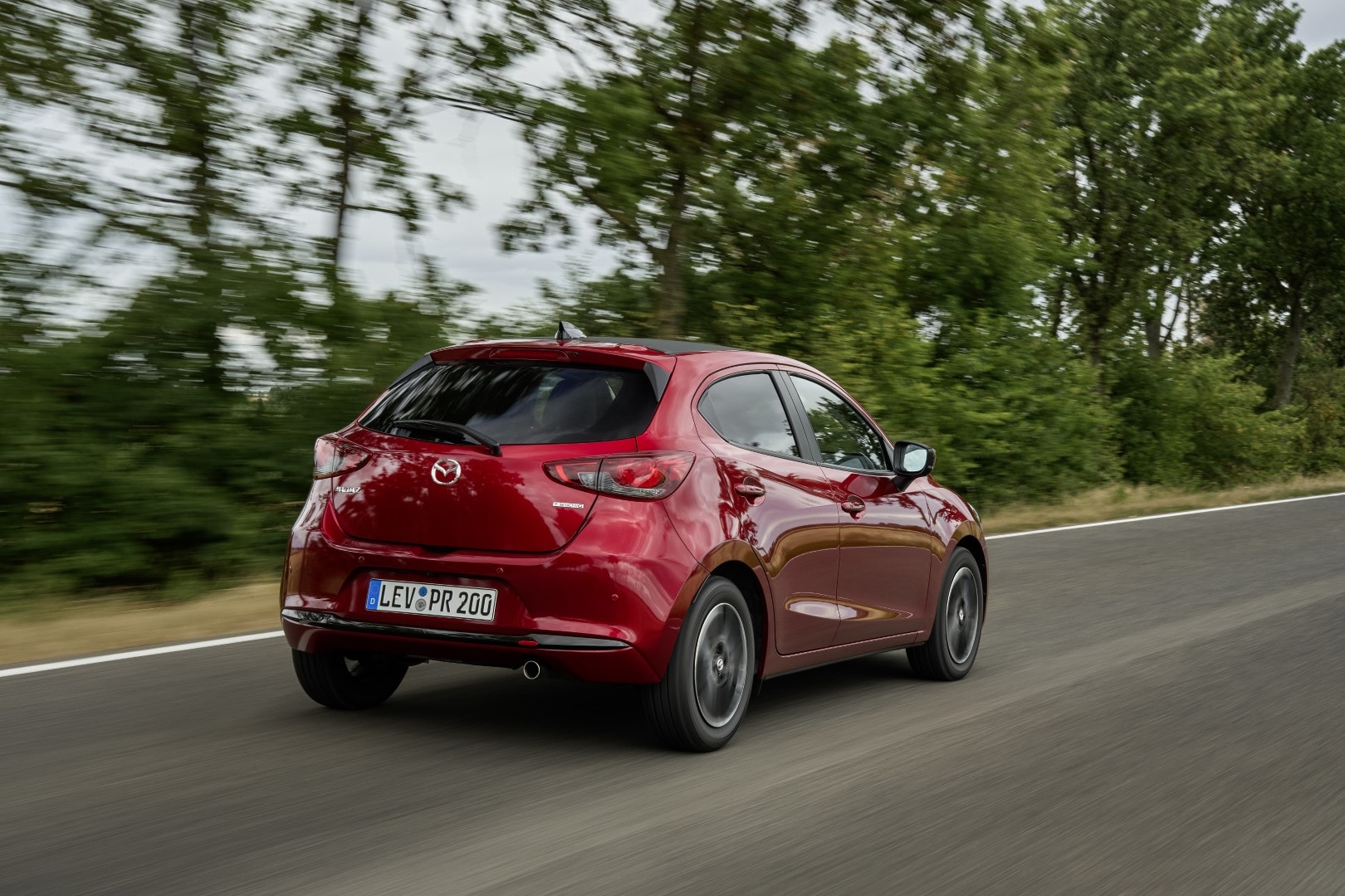 Perspectiva lateral del Mazda 2 circulando por una carretera rural.