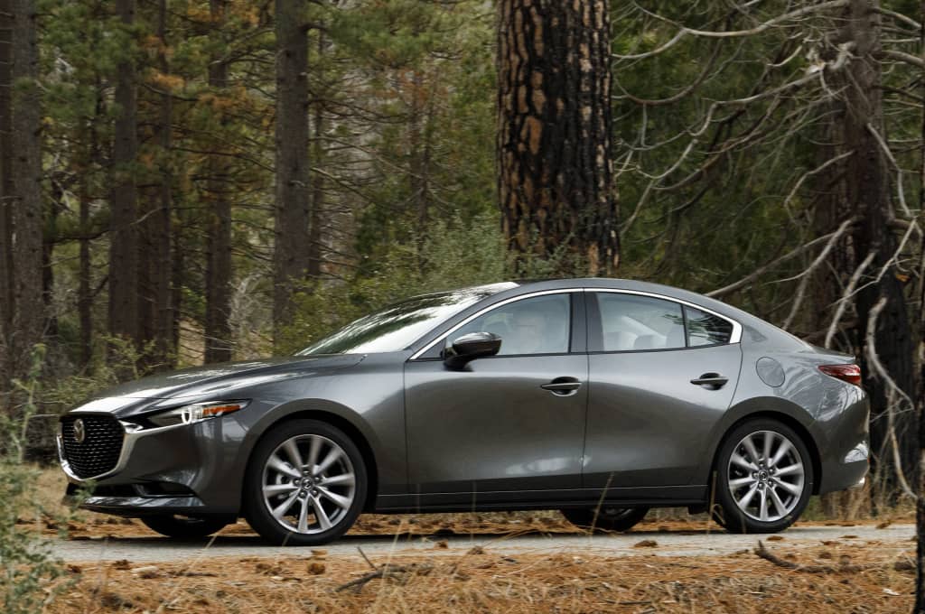 Vista lateral del Mazda 3 SportSedán en un entorno boscoso.