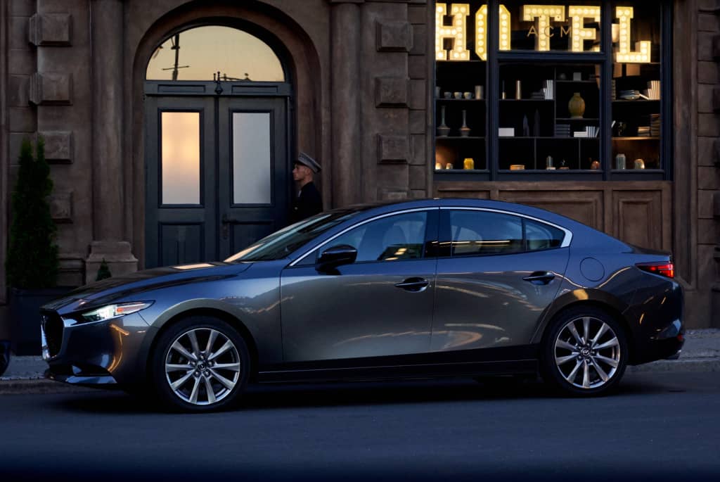 Lateral del Mazda 3 con un hotel de fondo, destacando su diseño.