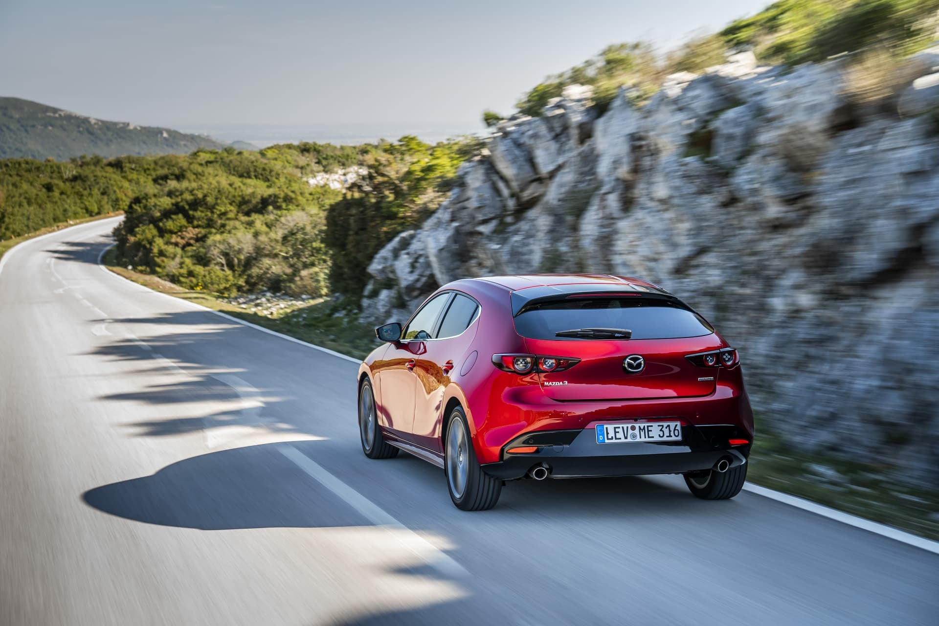 Vista trasera del Mazda 3 en carretera, destacando su diseño y deportividad.