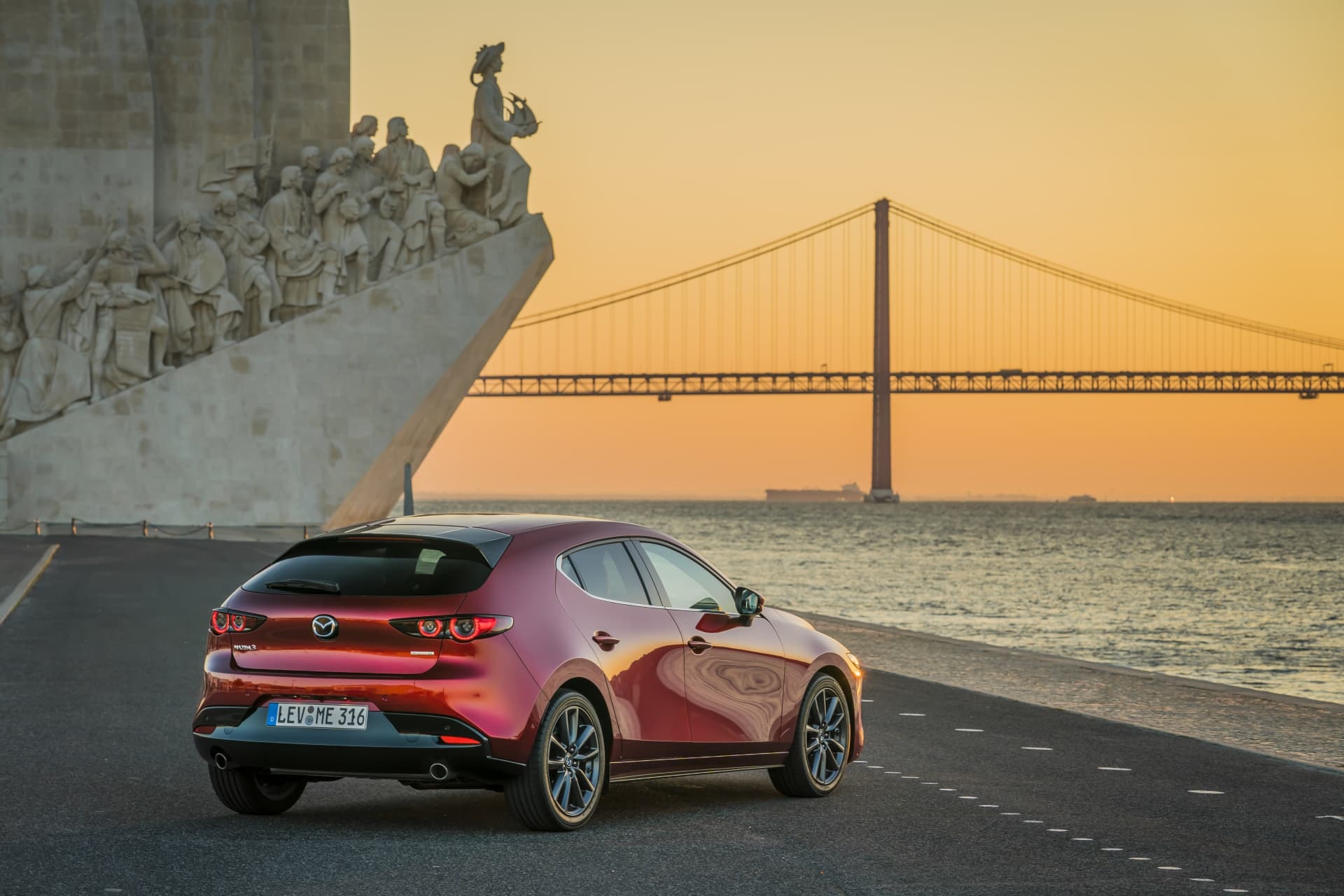 Elegante trasera del Mazda 3 con un monumento histórico al atardecer