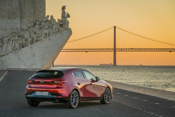 Elegante trasera del Mazda 3 con un monumento histórico al atardecer Elegante trasera del Mazda 3 con un monumento histórico al atardecer