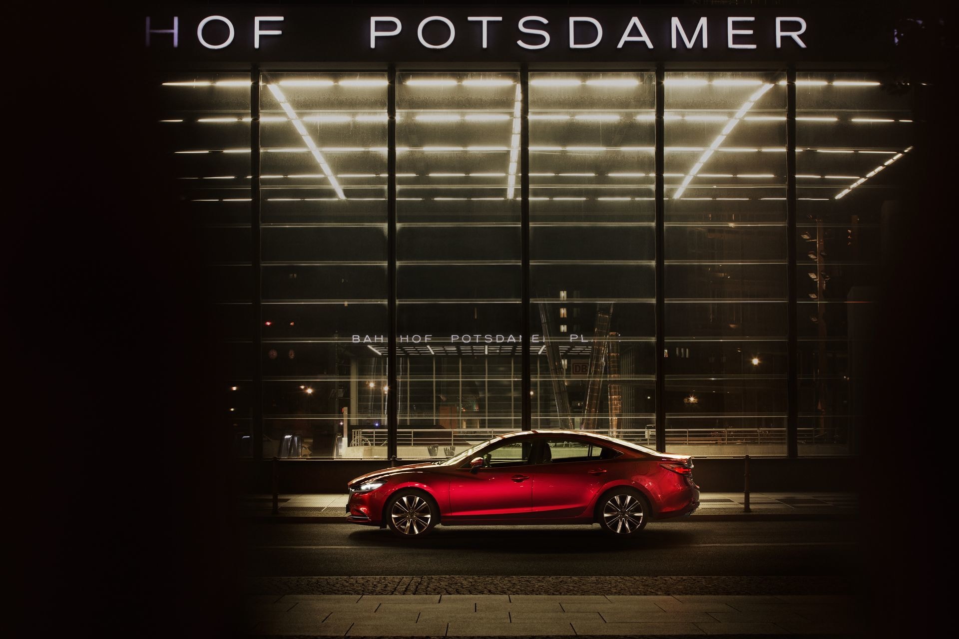 Perfil lateral de un Mazda 6 rojo iluminado por luces de ciudad de noche.