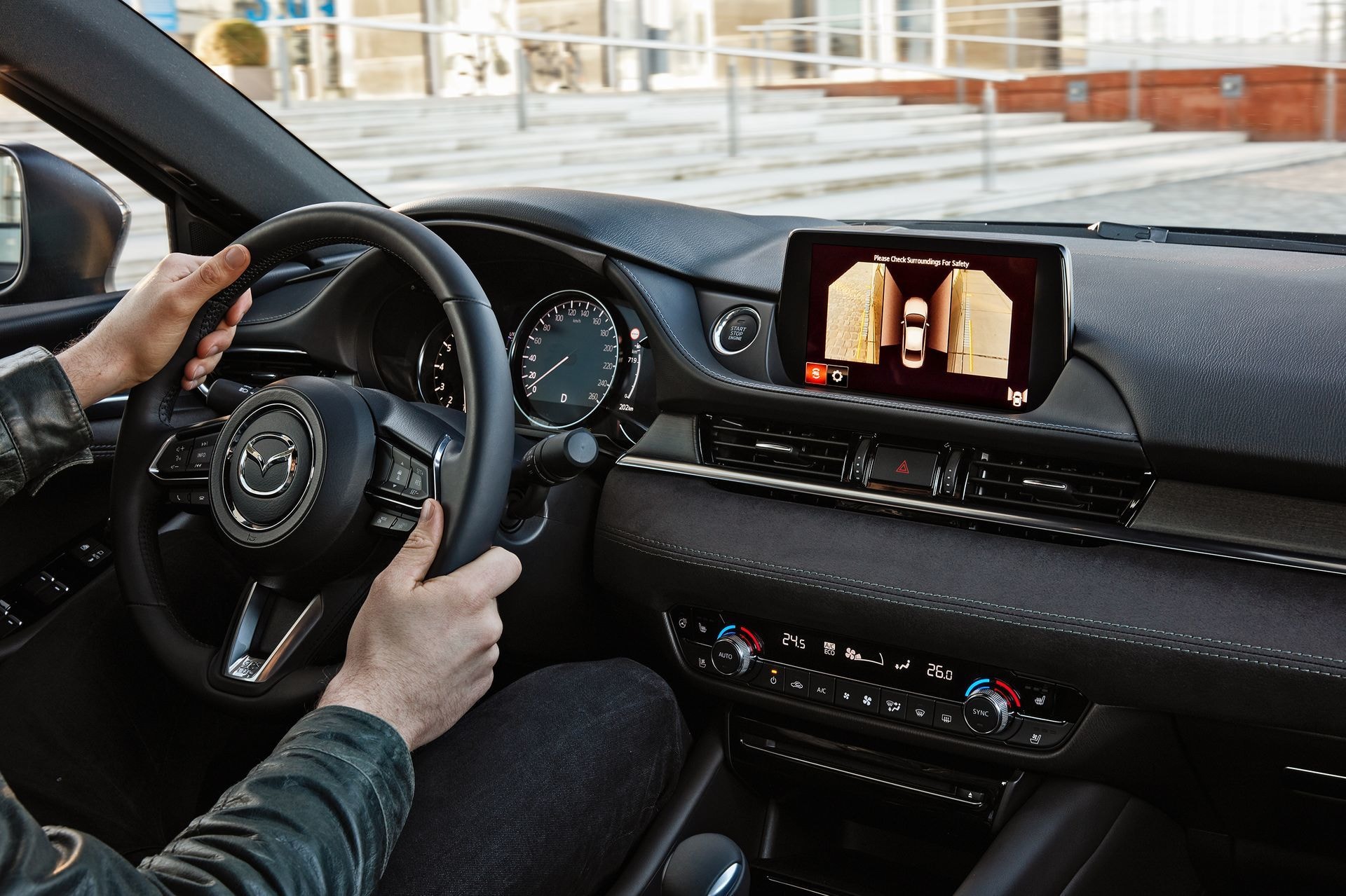 Conductor interactuando con el sistema de infotenimiento del Mazda 6, mostrando ergonomía.