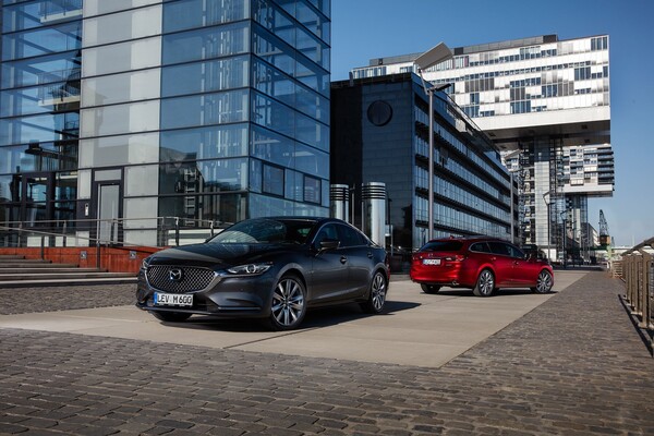 Dos Mazda 6, uno gris y otro rojo, en entorno urbano.