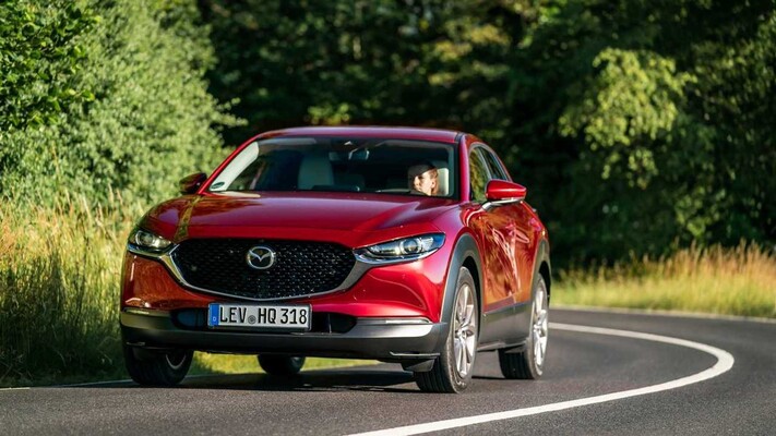 Vista dinámica del Mazda CX-30 en carretera, mostrando su diseño frontal y perfil lateral. Vista dinámica del Mazda CX-30 en carretera, mostrando su diseño frontal y perfil lateral.