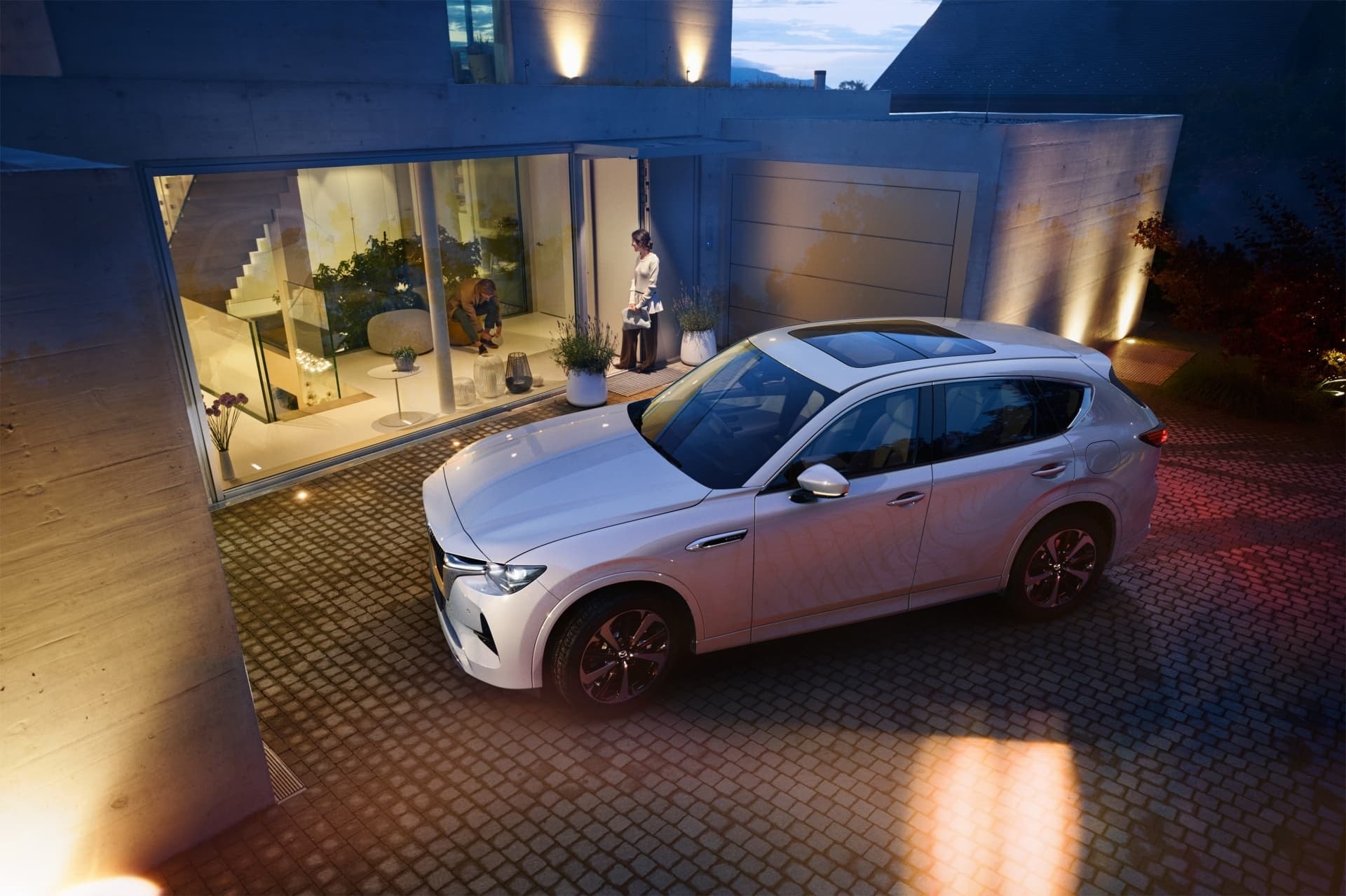 Vista nocturna del Mazda CX-60 frente a una residencia moderna.