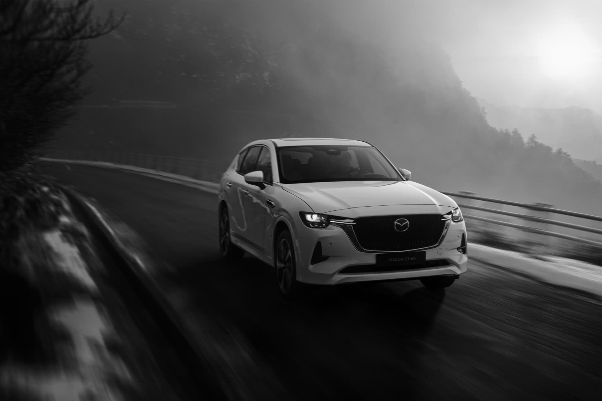 Captura en blanco y negro del CX-60, resaltando su frente mientras se desplaza en la carretera.