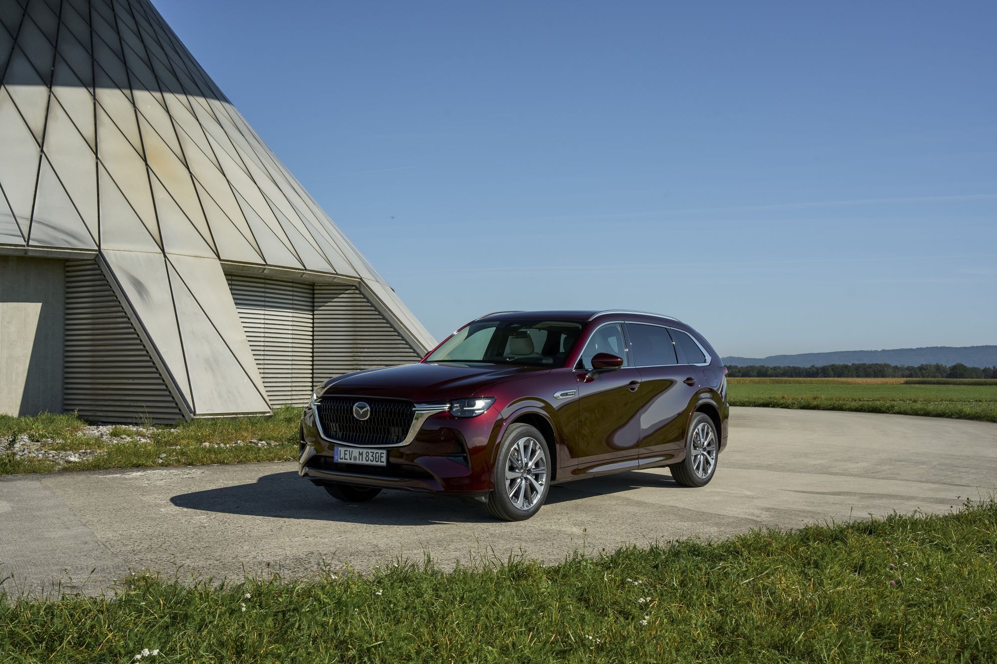 Vista trasera del Mazda CX-80 con una estructura interesante al fondo.