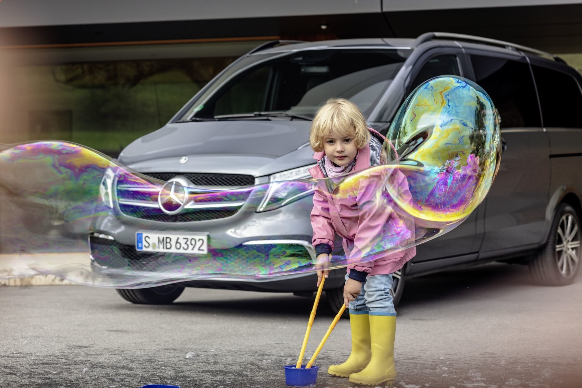 Imagen lúdica con un Mercedes Clase V al fondo y una niña jugando con burbujas.