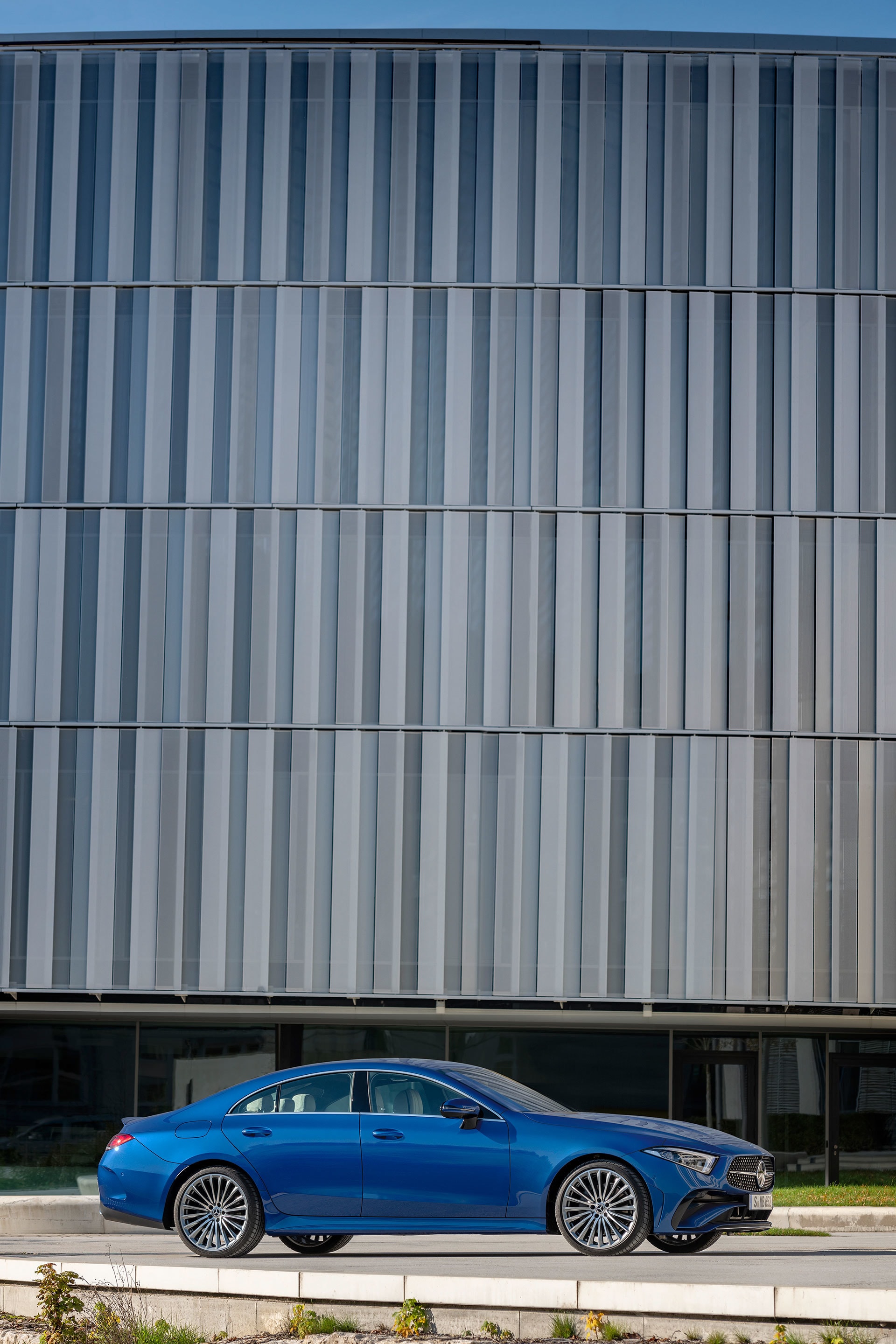 Mercedes CLS estacionado ante arquitectura contemporánea, énfasis en diseño lateral.