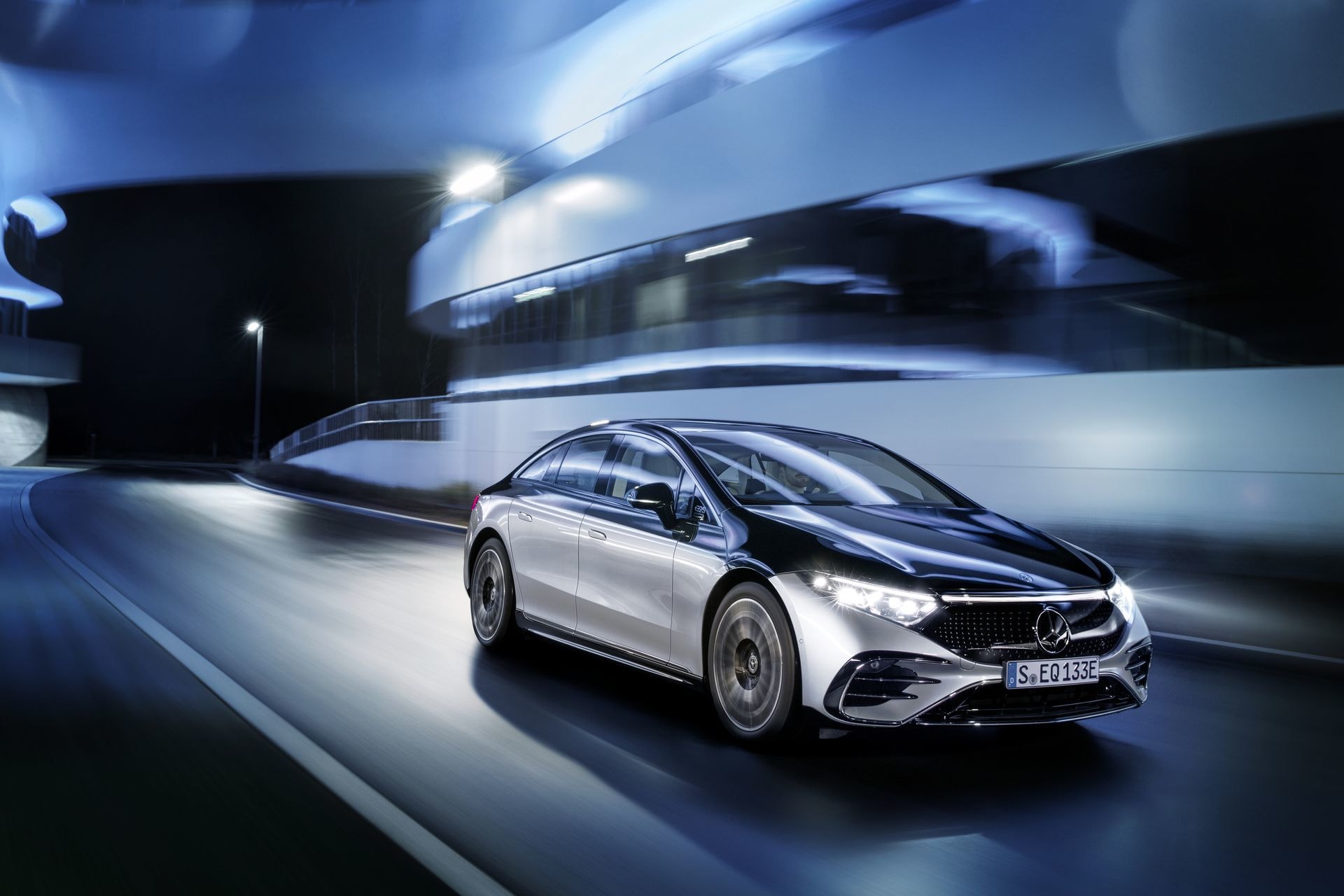 Mercedes EQS en velocidad con luces de ciudad al fondo, exhibiendo su estilismo lateral.