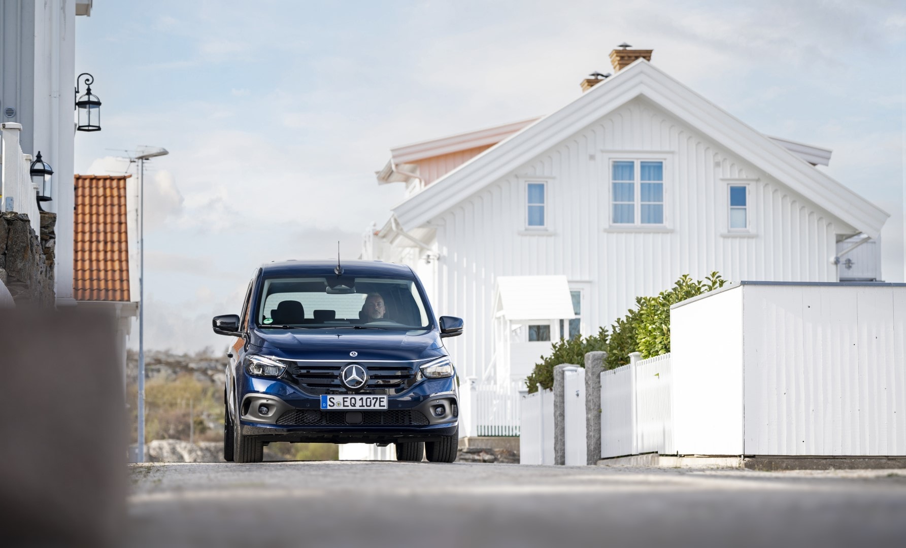 Presentación del frente del Mercedes EQT con una casa de fondo, ilustrando su carácter familiar.