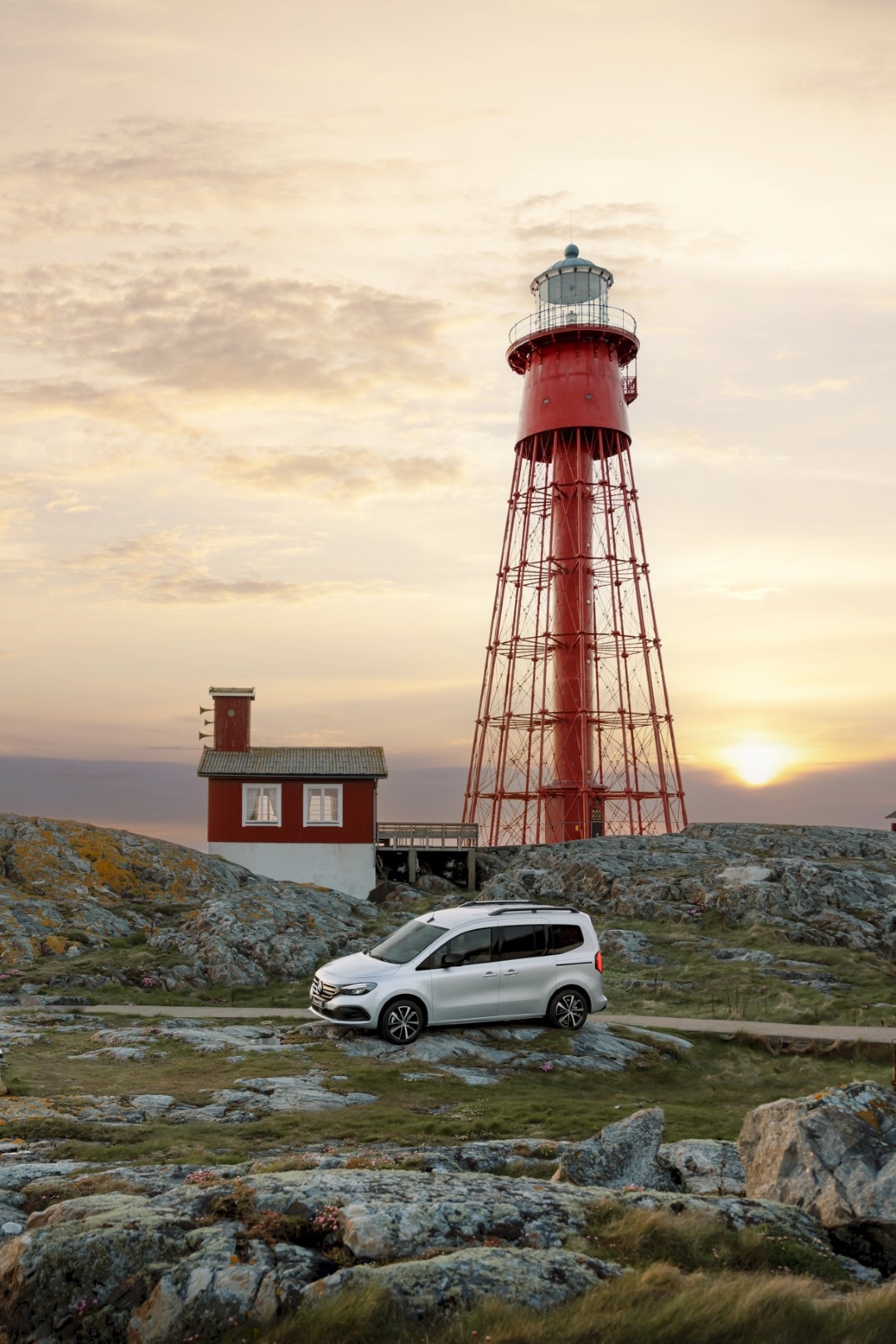 Vista lateral con énfasis en el techo del Mercedes EQT junto a un faro al atardecer.