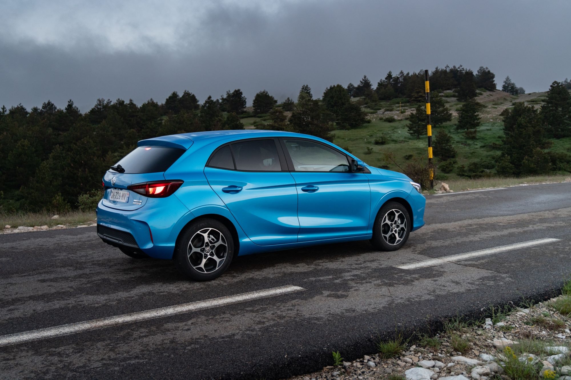 Perspectiva lateral del MG 3 en una carretera de montaña, combinando elegancia y deportividad.