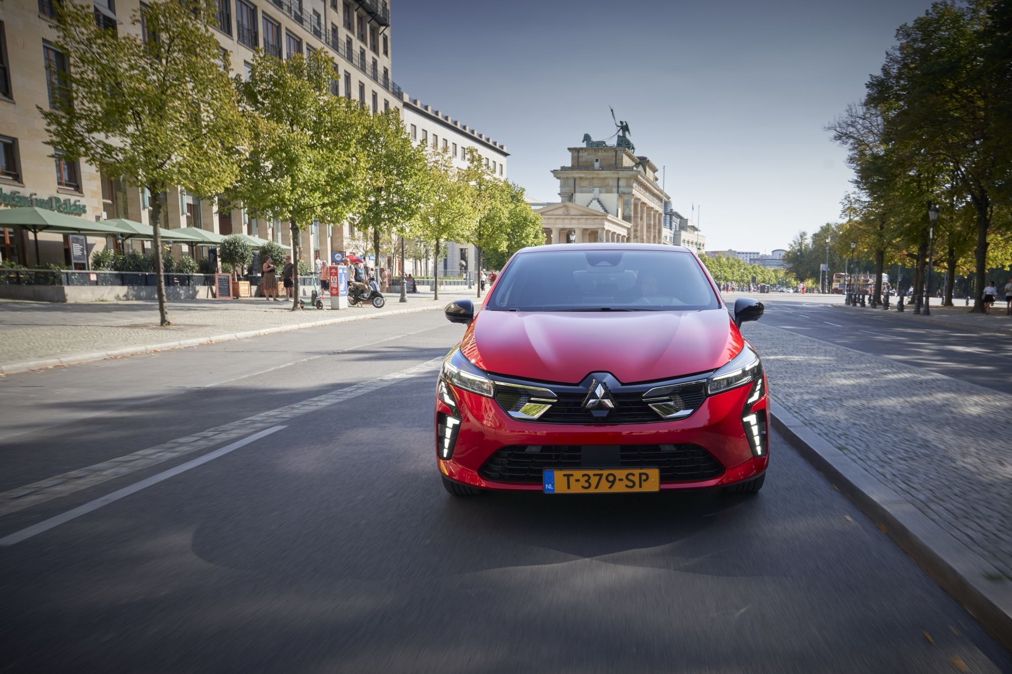 Primer plano del frente del Mitsubishi Colt híbrido con un trasfondo histórico.