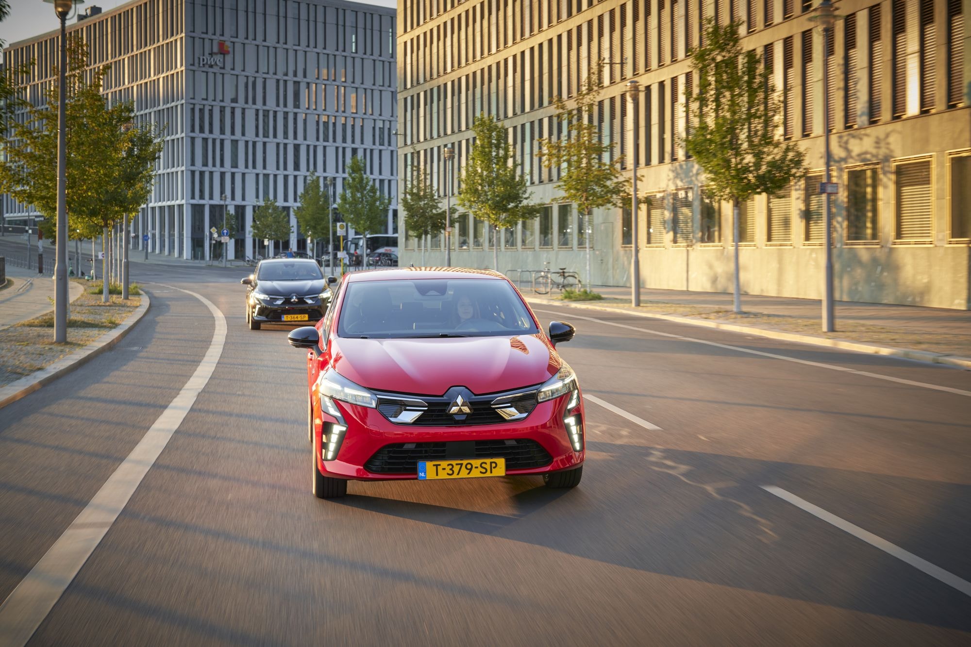 Mitsubishi Colt híbrido recorriendo una moderna vía urbana al caer la tarde.