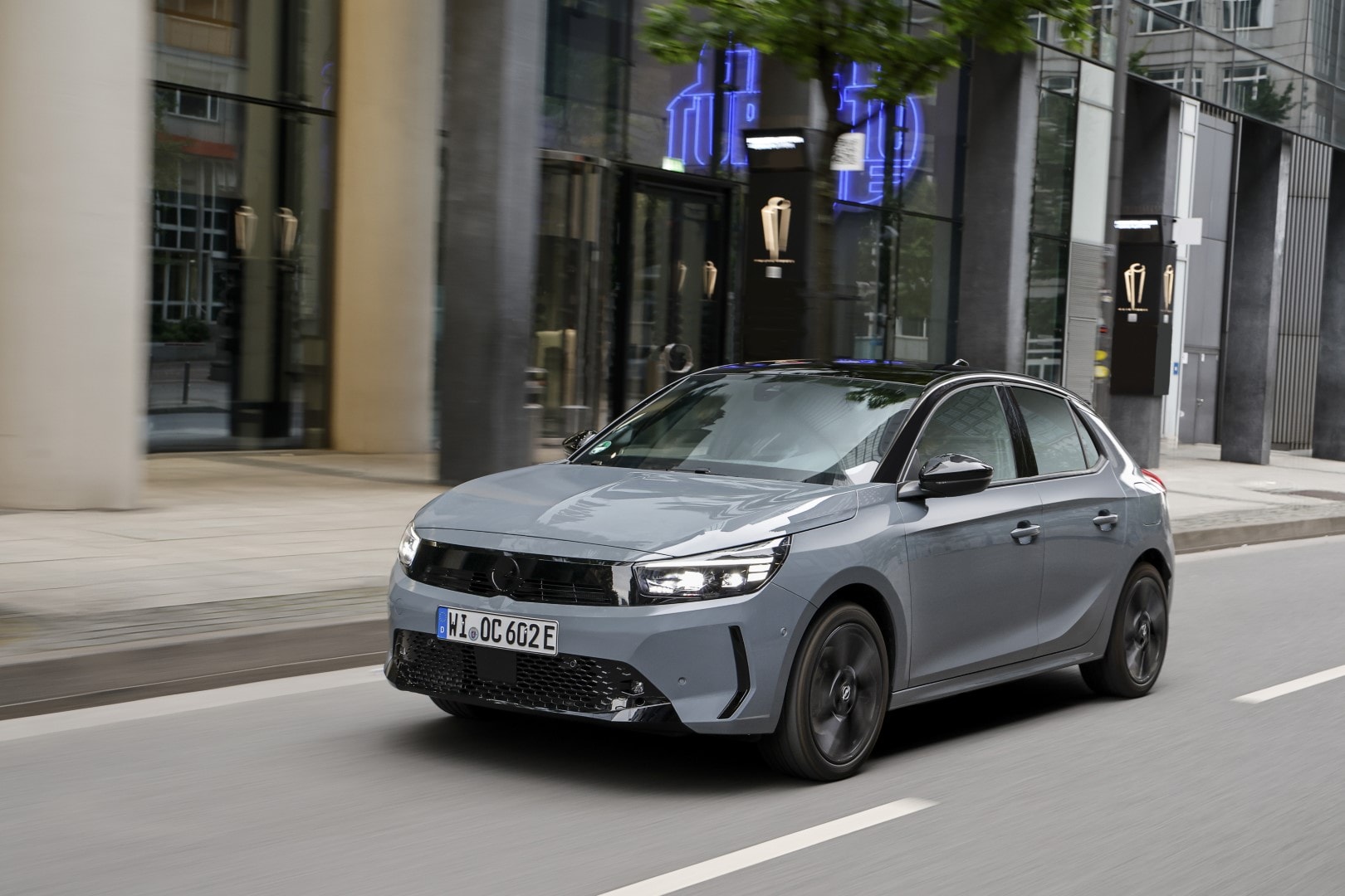 Vista lateral y parcialmente delantera del Opel Corsa-e circulando por la ciudad.