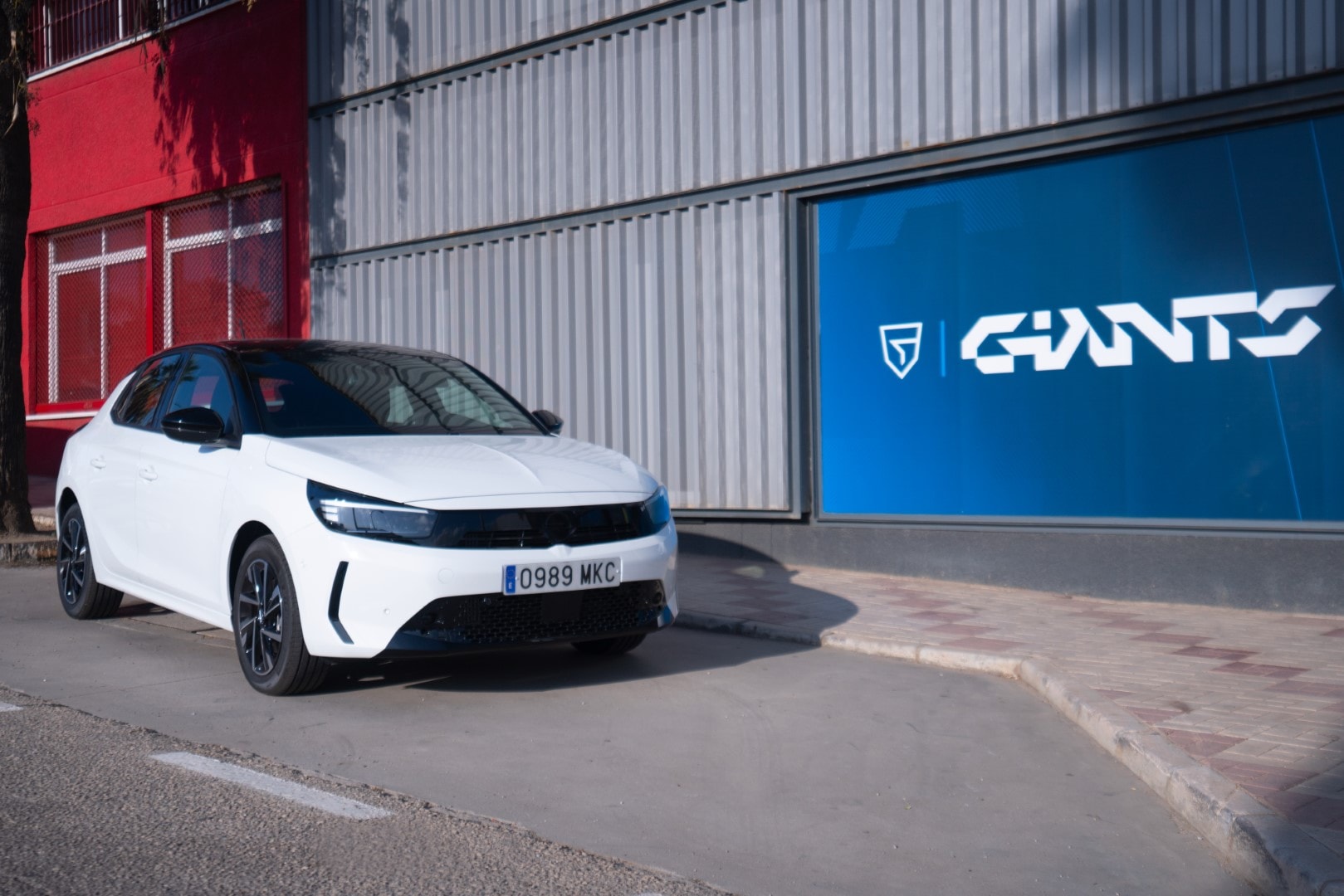 Vista angular delantero-lateral del Corsa-e frente a logos empresariales.