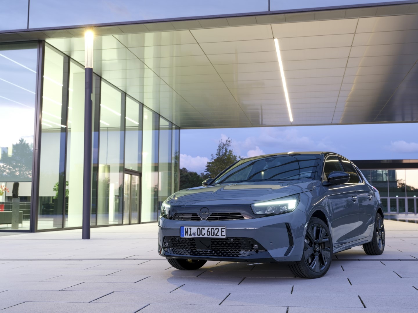 Vista frontal del Corsa-e destacando su diseño de iluminación frente a arquitectura de vidrio.
