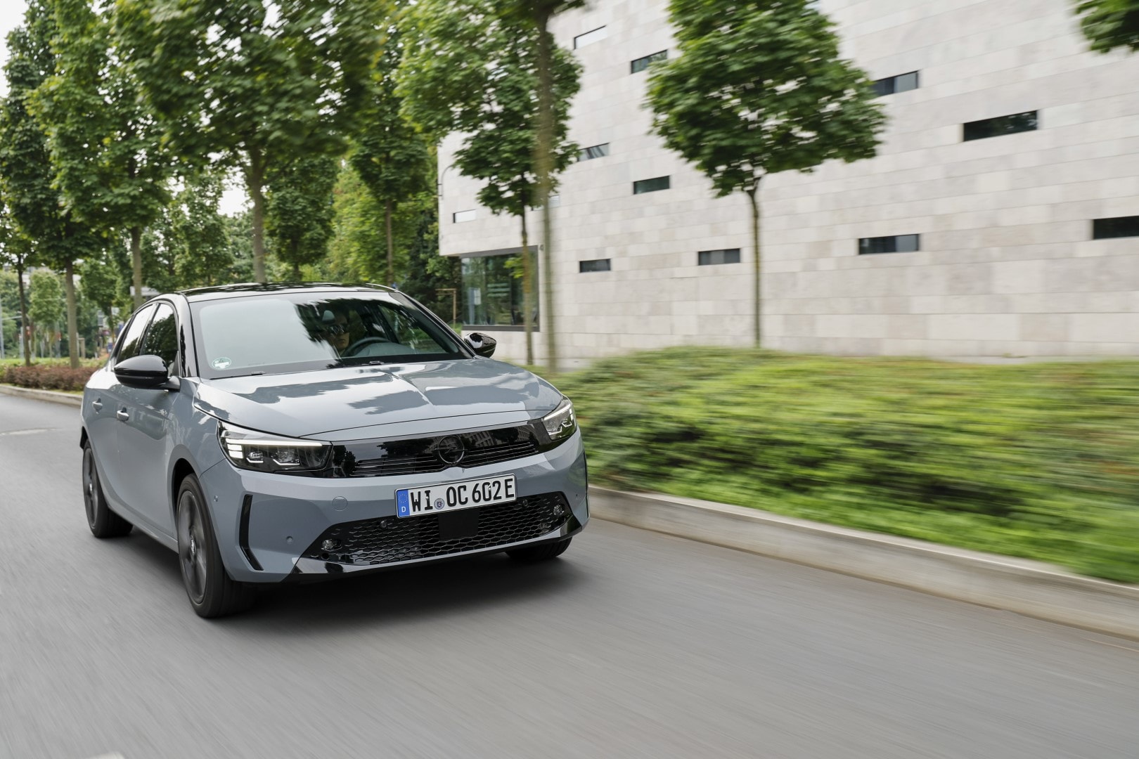 Imagen lateral del Opel Corsa-e circulando cerca de edificios modernos.