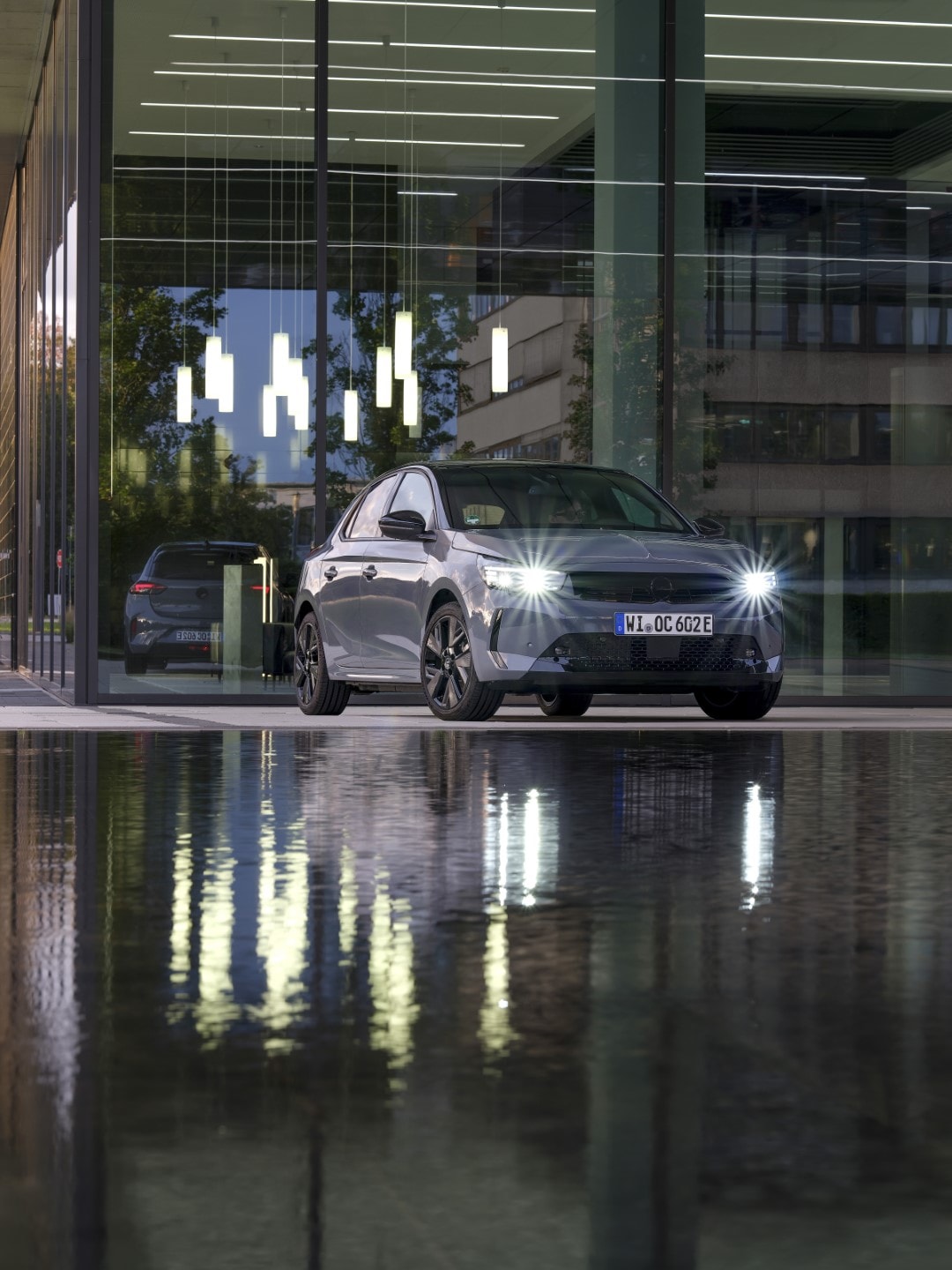 Vista nocturna del Opel Corsa-e reflejándose sobre el suelo mojado.