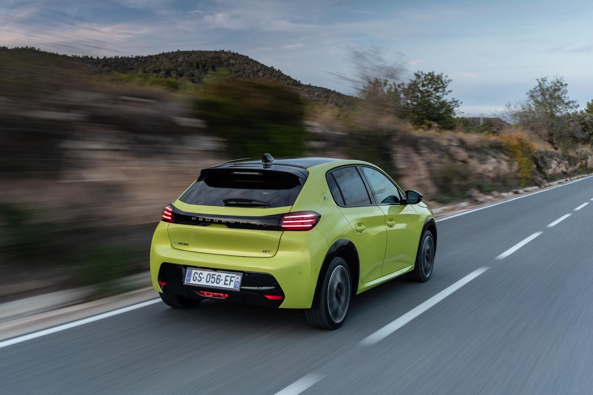 Vista dinámica del Peugeot e-208 en carretera, destacando su diseño fluido.