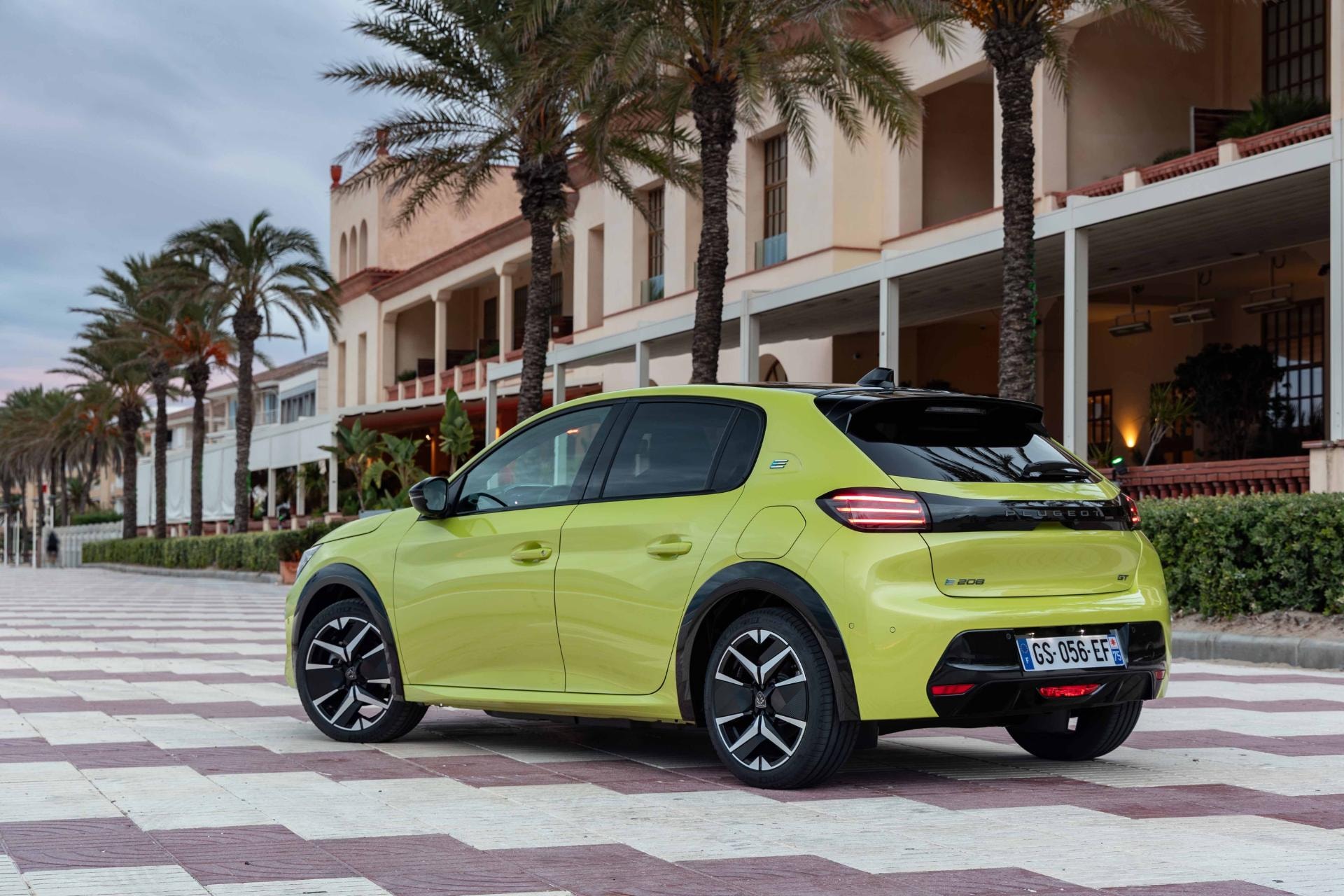 Peugeot e-208 aparcado, mostrando su línea trasera y lateral en un entorno urbano.