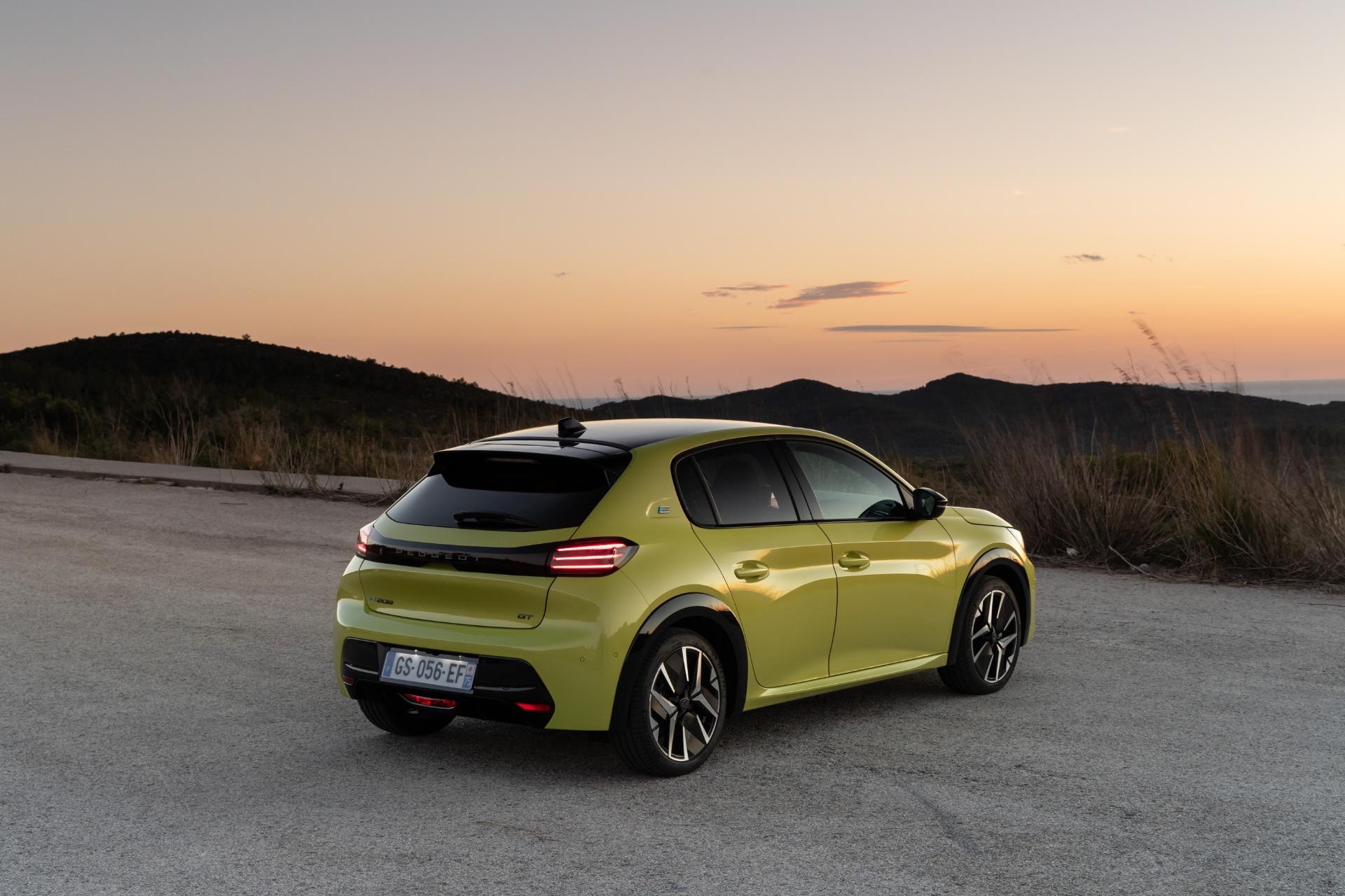Imagen que muestra trasera y perfil del Peugeot e-208 al atardecer.