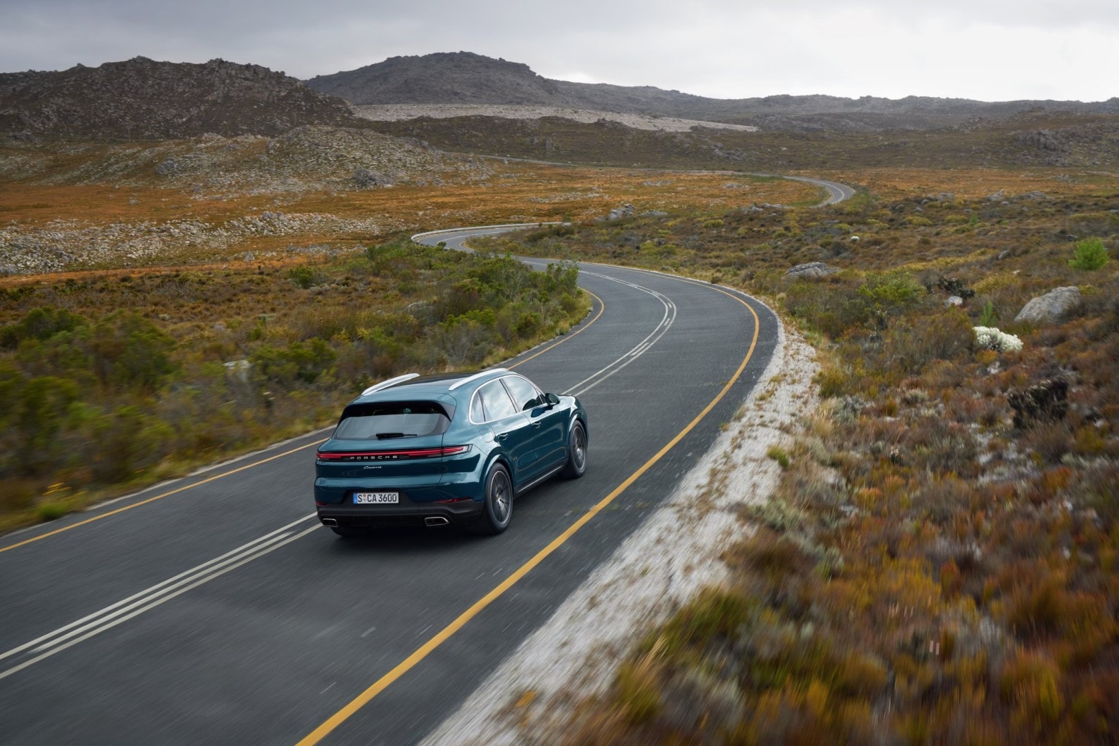 Vista trasera del Porsche Cayenne en carretera de montaña, destacando su diseño y deportividad.