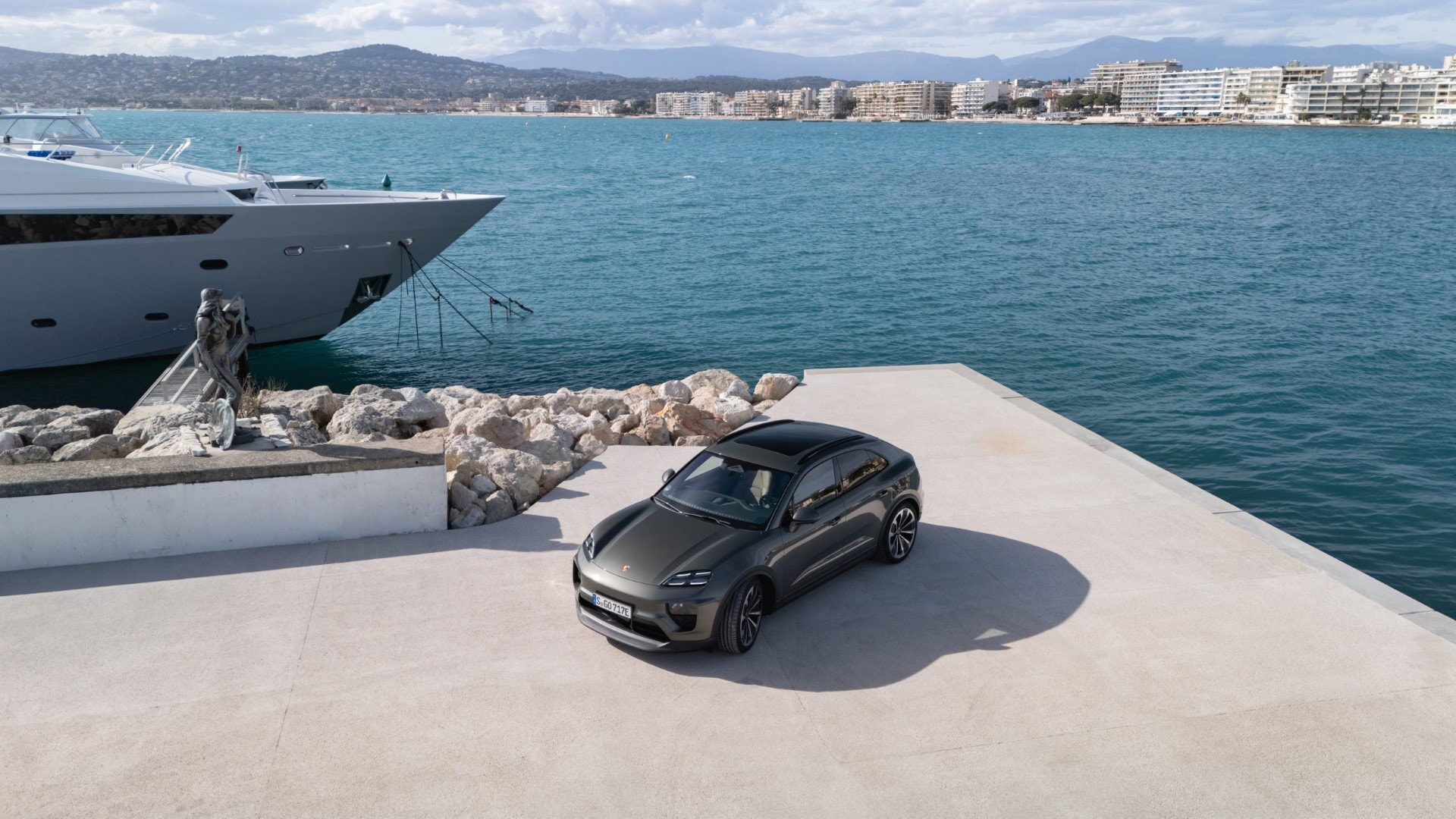 Vista lateral del Porsche Macan aparcado en un muelle junto a yates de lujo.