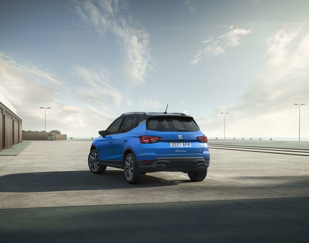 Vista trasera y lateral del SEAT Arona azul, evidenciando sus ópticas y diseño posterior. Vista trasera y lateral del SEAT Arona azul, evidenciando sus ópticas y diseño posterior.