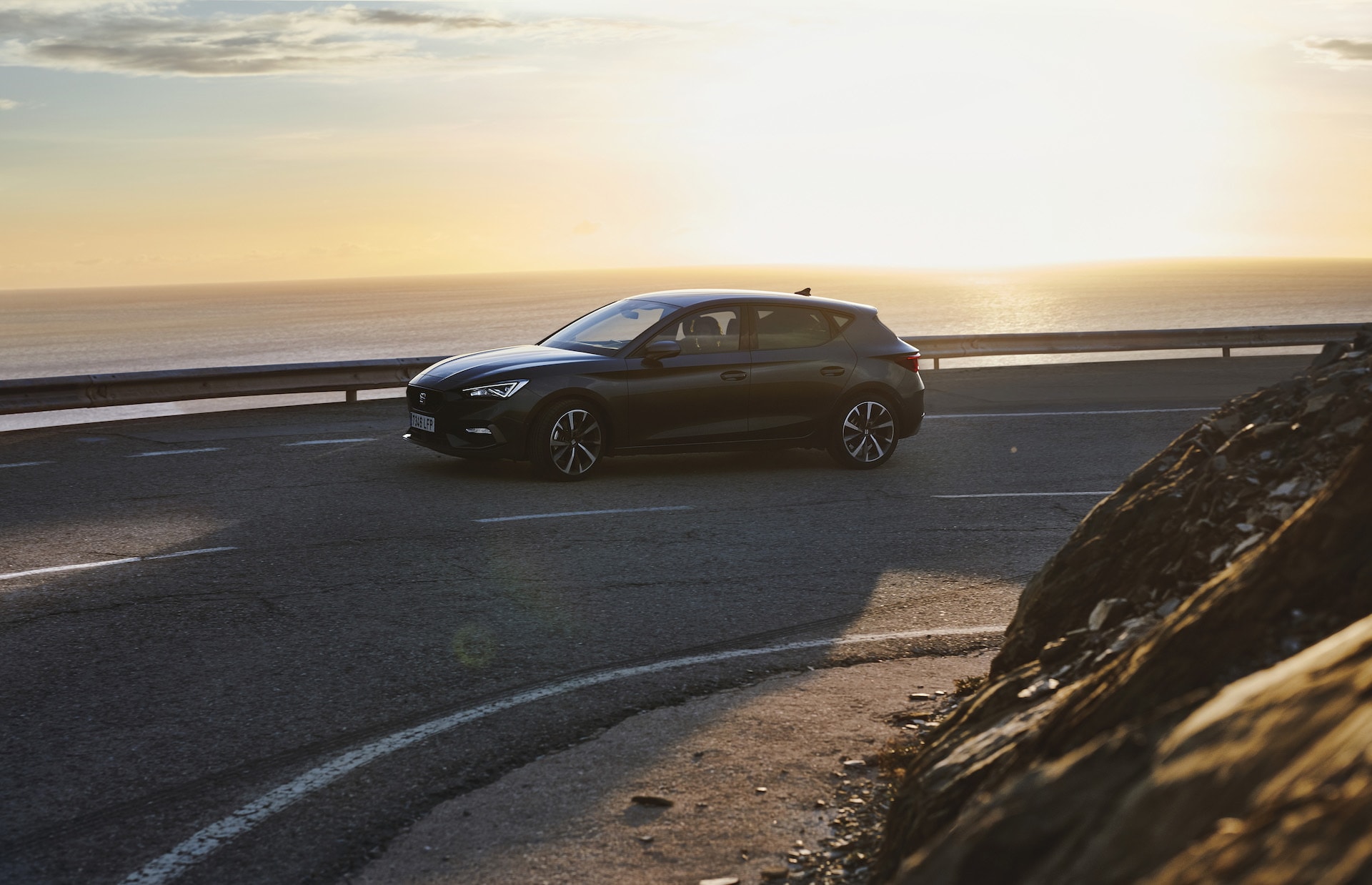 SEAT León negro ante un impresionante paisaje costero al atardecer.