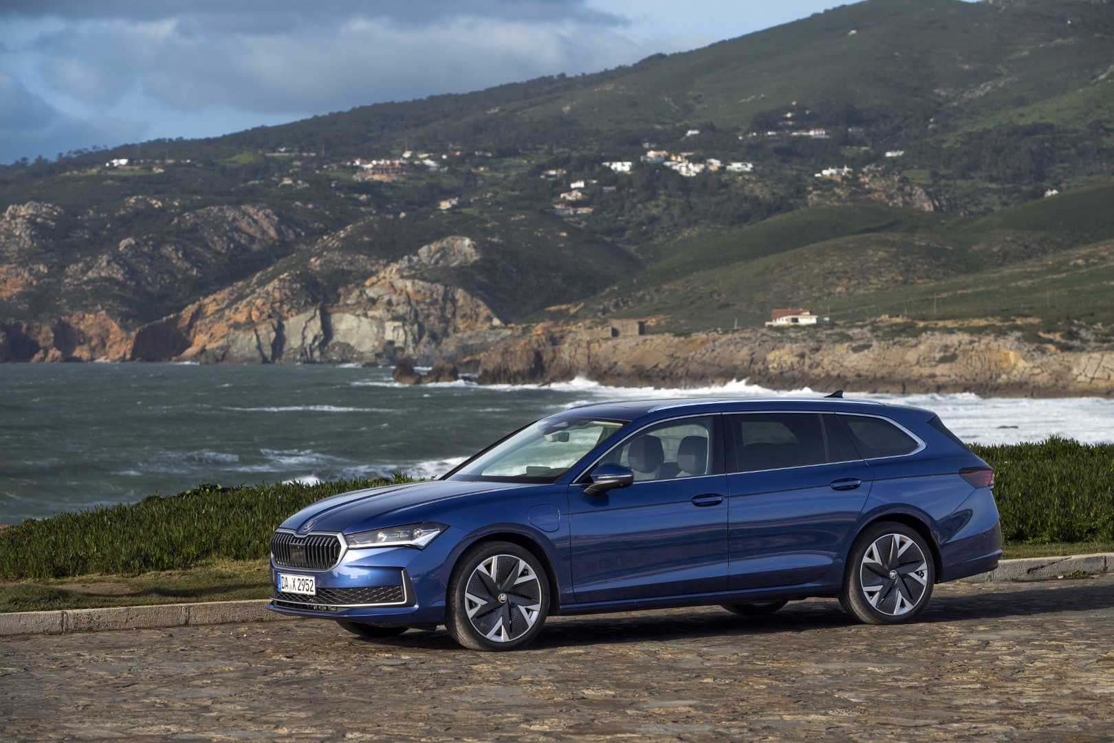 Vista diagonal delantera del Skoda Superb Combi contrastando con un paisaje costero.