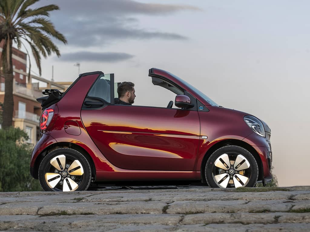 Silueta del Smart EQ Fortwo Cabrio en rojo al atardecer, techo retráctil abierto.