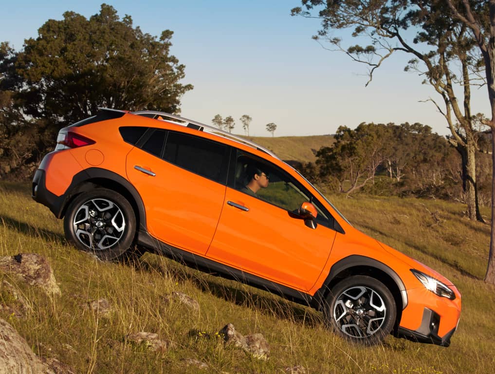 Vista lateral del Subaru XV naranja escalando una ladera, exhibiendo sus llantas y líneas.