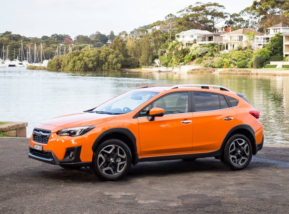 Perfil lateral del Subaru XV color naranja situado en un entorno de puerto.