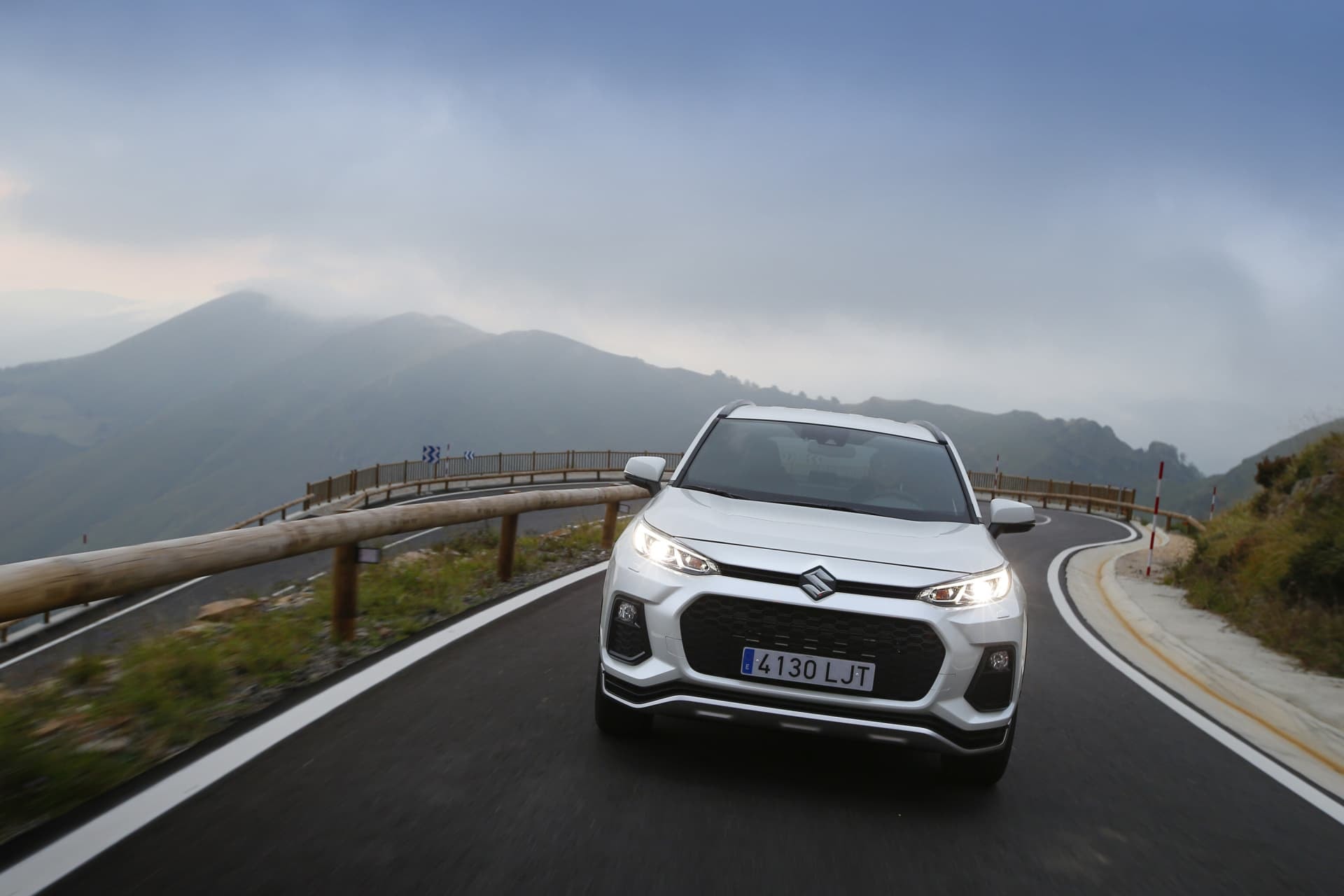 Suzuki Across híbrido tomando una curva con la carretera de fondo.