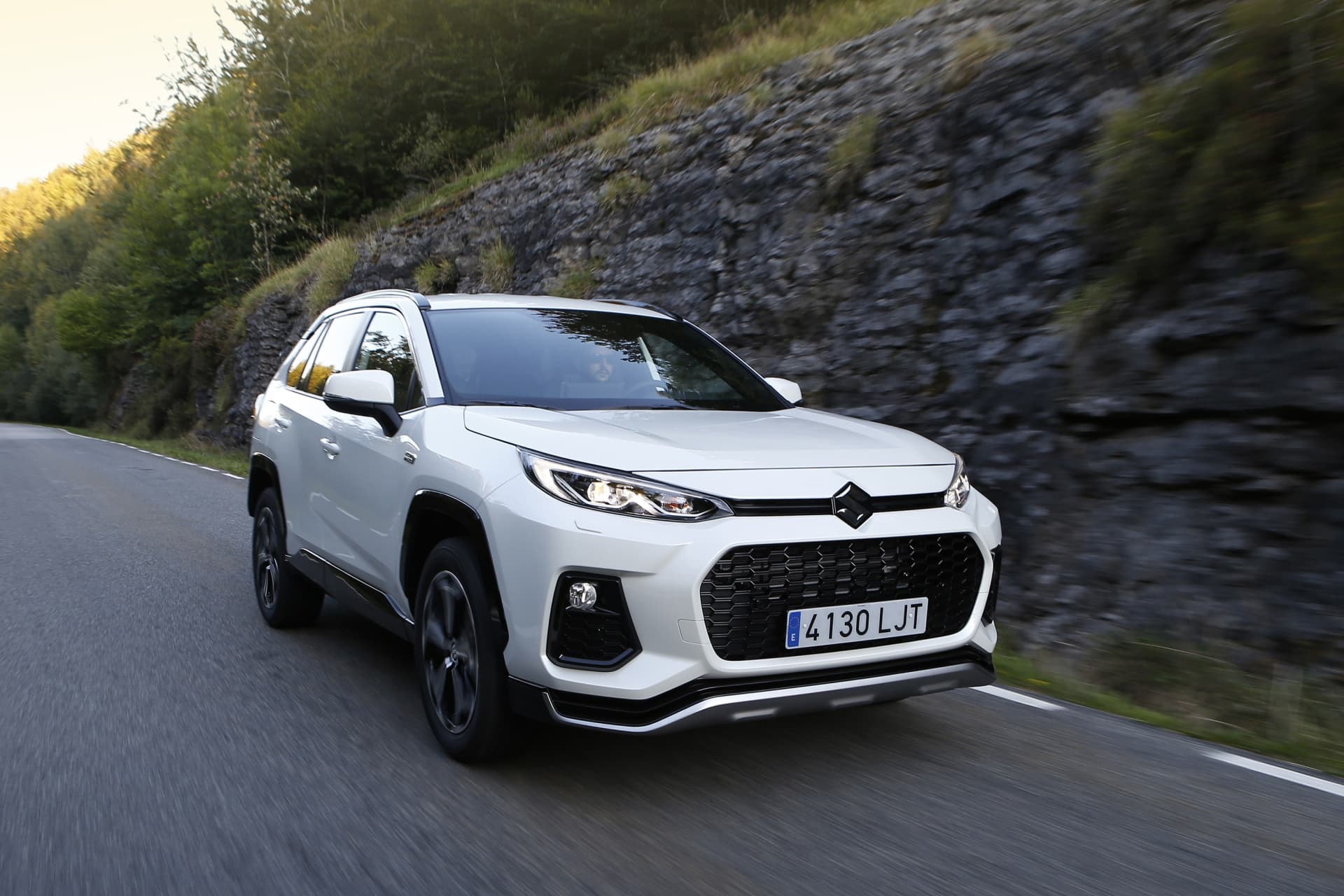 Suzuki Across híbrido capturado en acción en un entorno de carretera montañosa.