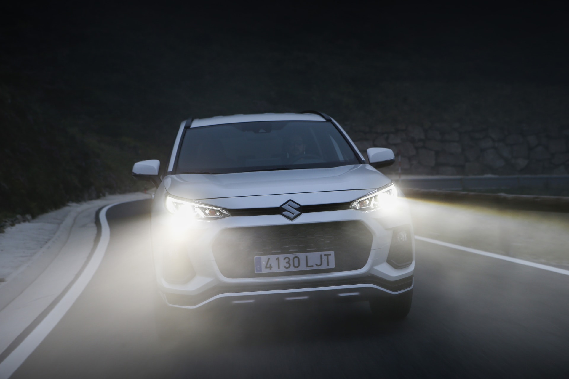 Suzuki Across mostrando su frontal con luces LED encendidas durante el crepúsculo.