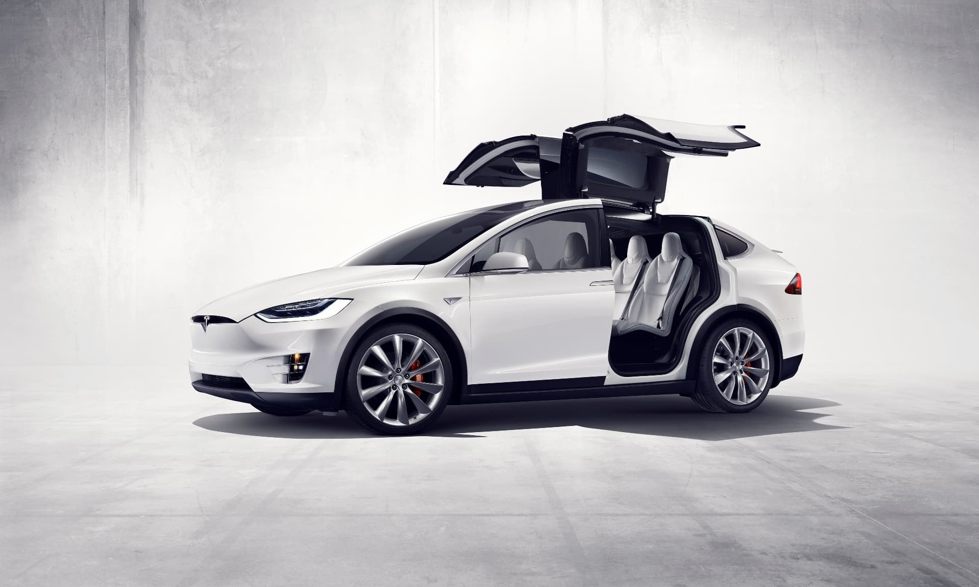 Tesla Model X blanco con puertas tipo falcon wings abiertas en estudio.