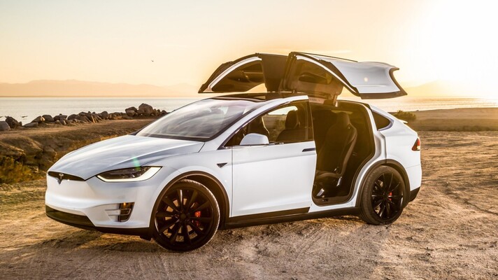 Model X mostrando puertas tipo falcon wings abiertas al atardecer.