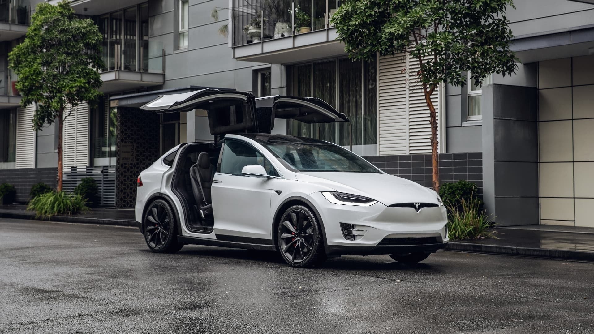 Tesla Model X con puertas tipo falcon wings abiertas en entorno urbano.